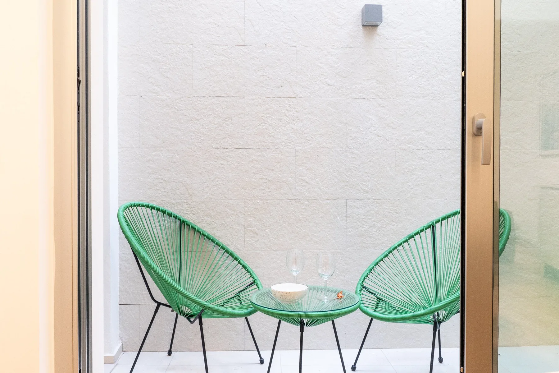 Una pequeña zona exterior para sentarse, con sillas verdes tejidas y una mesa redonda.