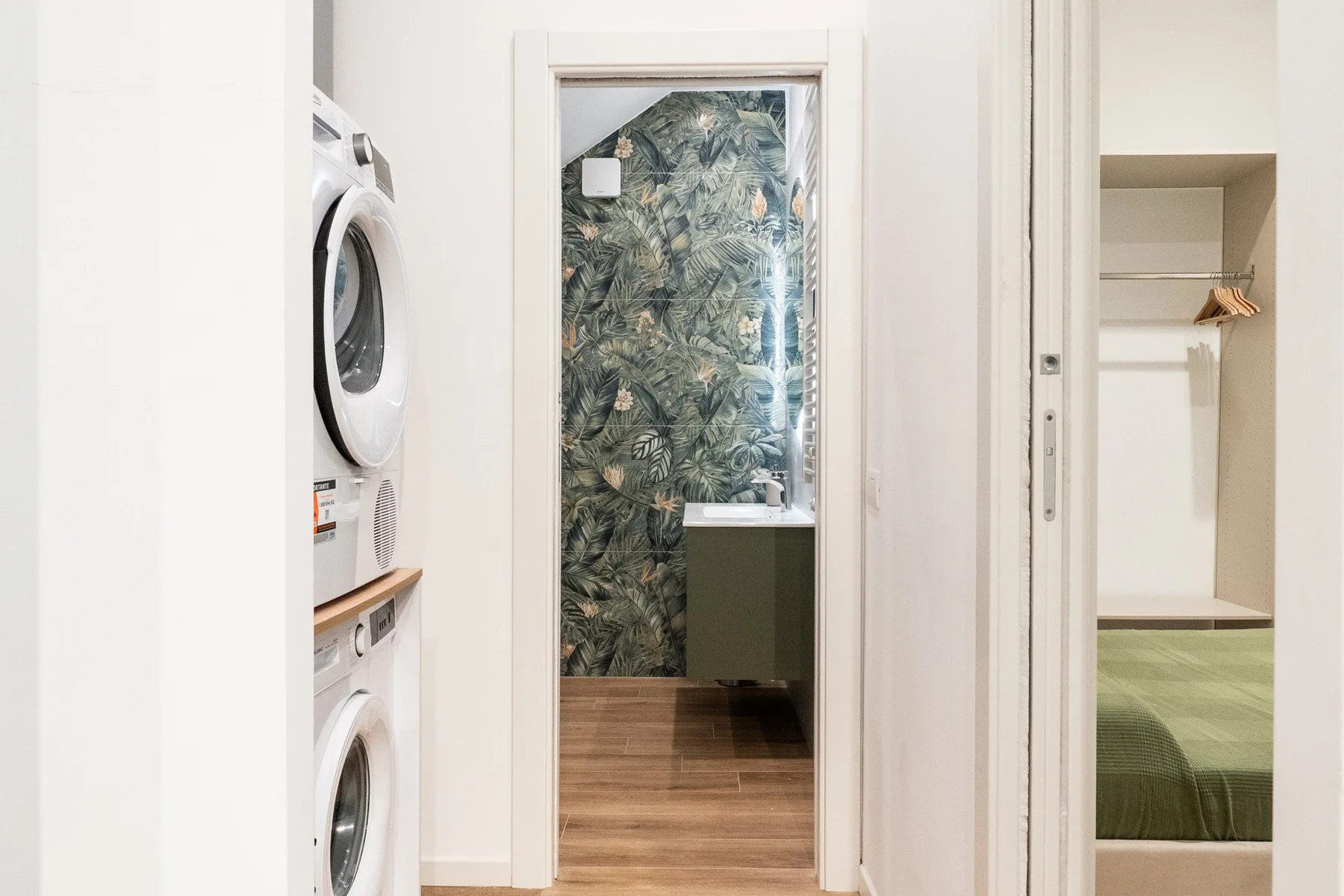 Un pasillo da a una zona de lavandería con electrodomésticos apilados y un dormitorio.