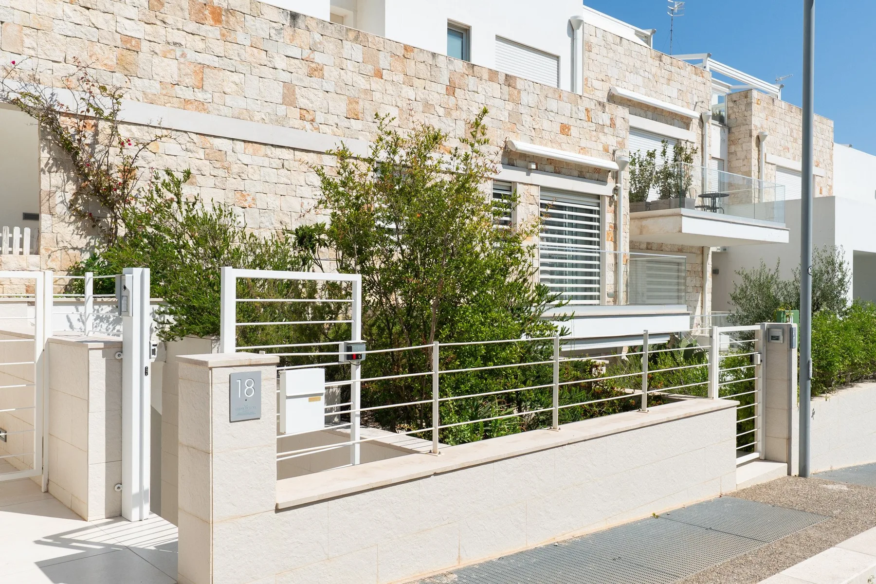 Un edificio residencial moderno con fachada de piedra, balcones y jardín delantero.