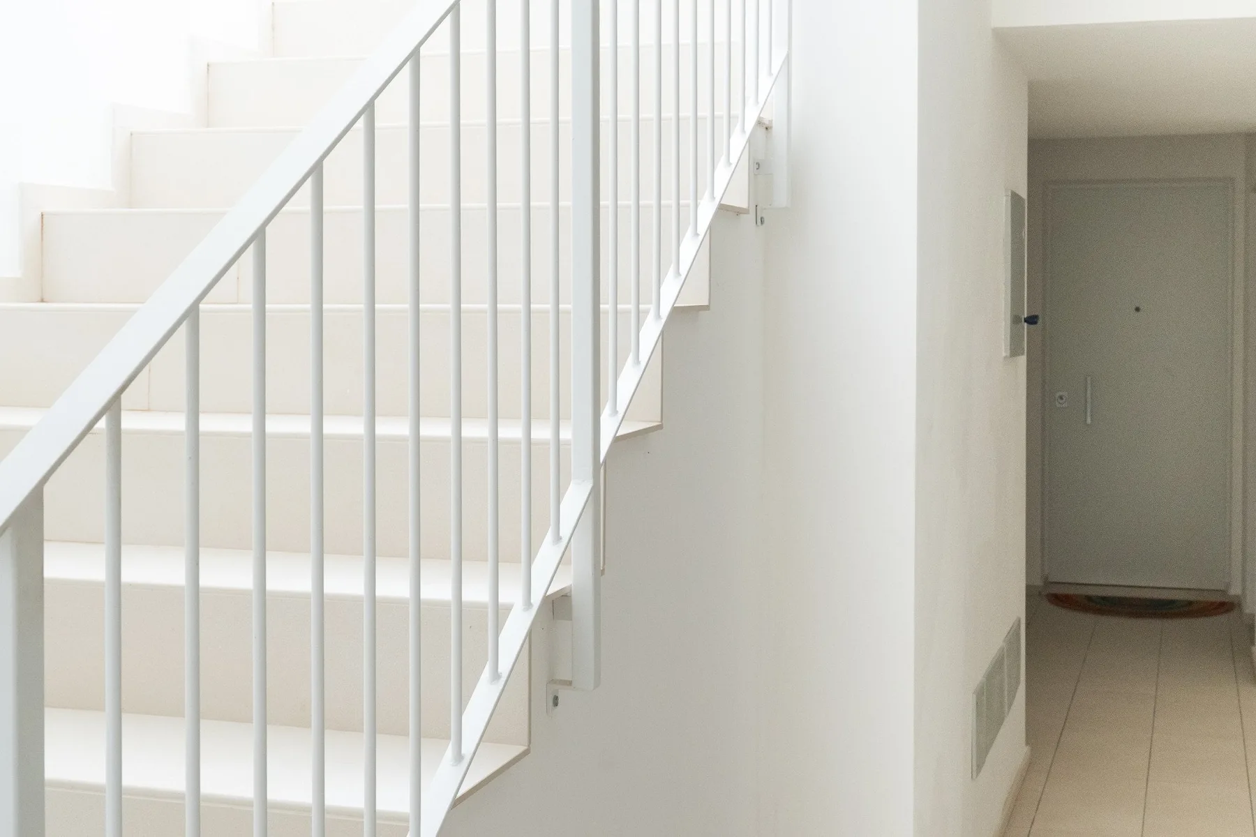 Una escalera interior luminosa con barandilla blanca junto a un pasillo.