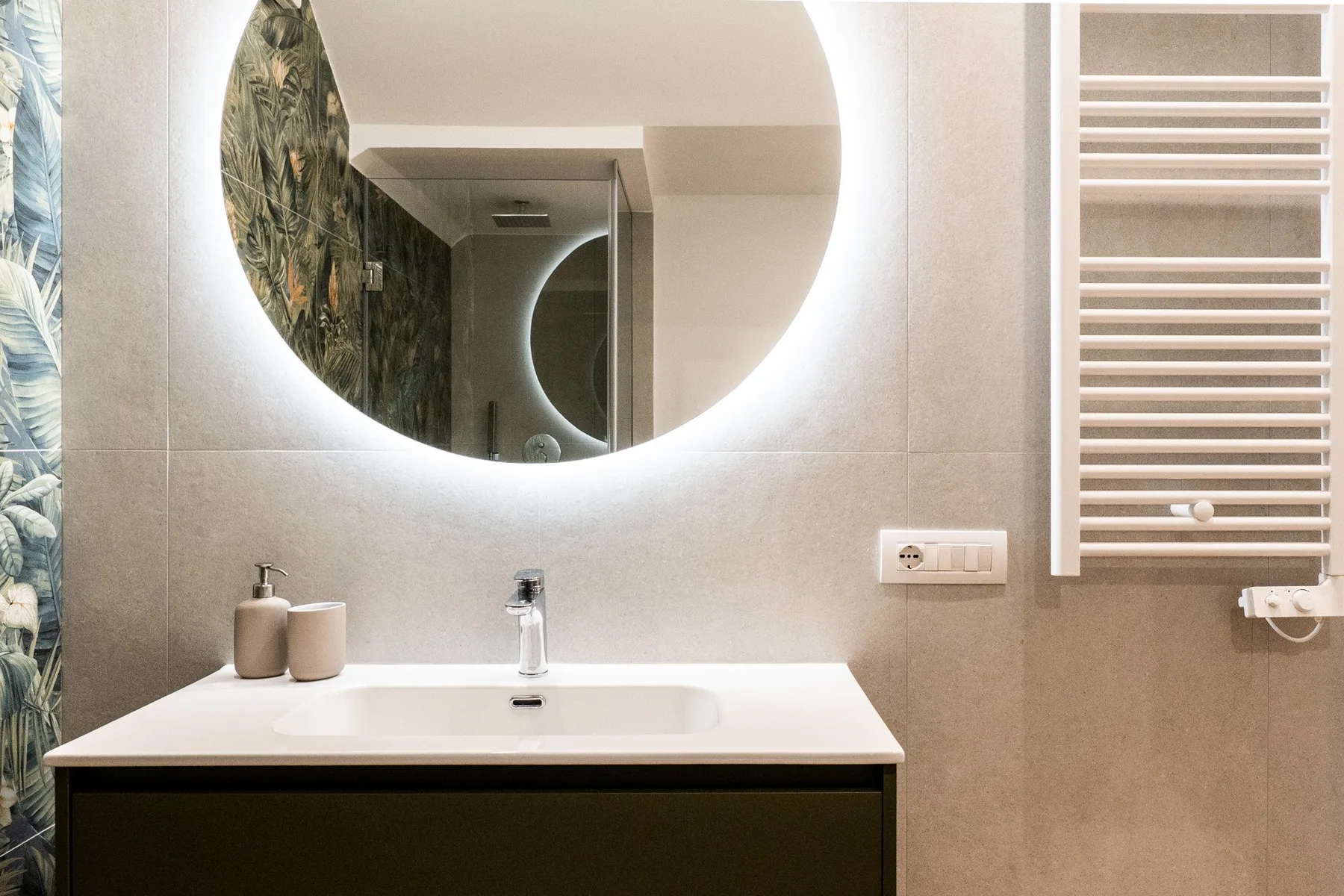 Un lavabo de baño con un espejo redondo y un toallero calefactable.