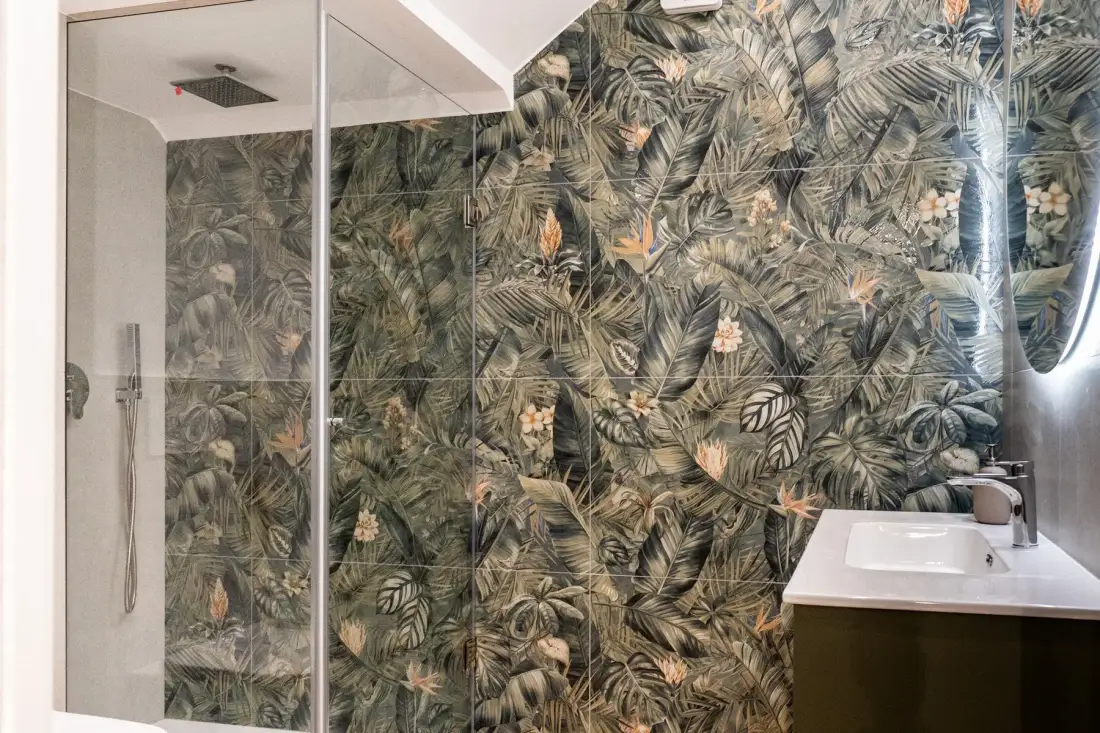 Un baño con una ducha de vidrio y una pared con motivos de hojas.