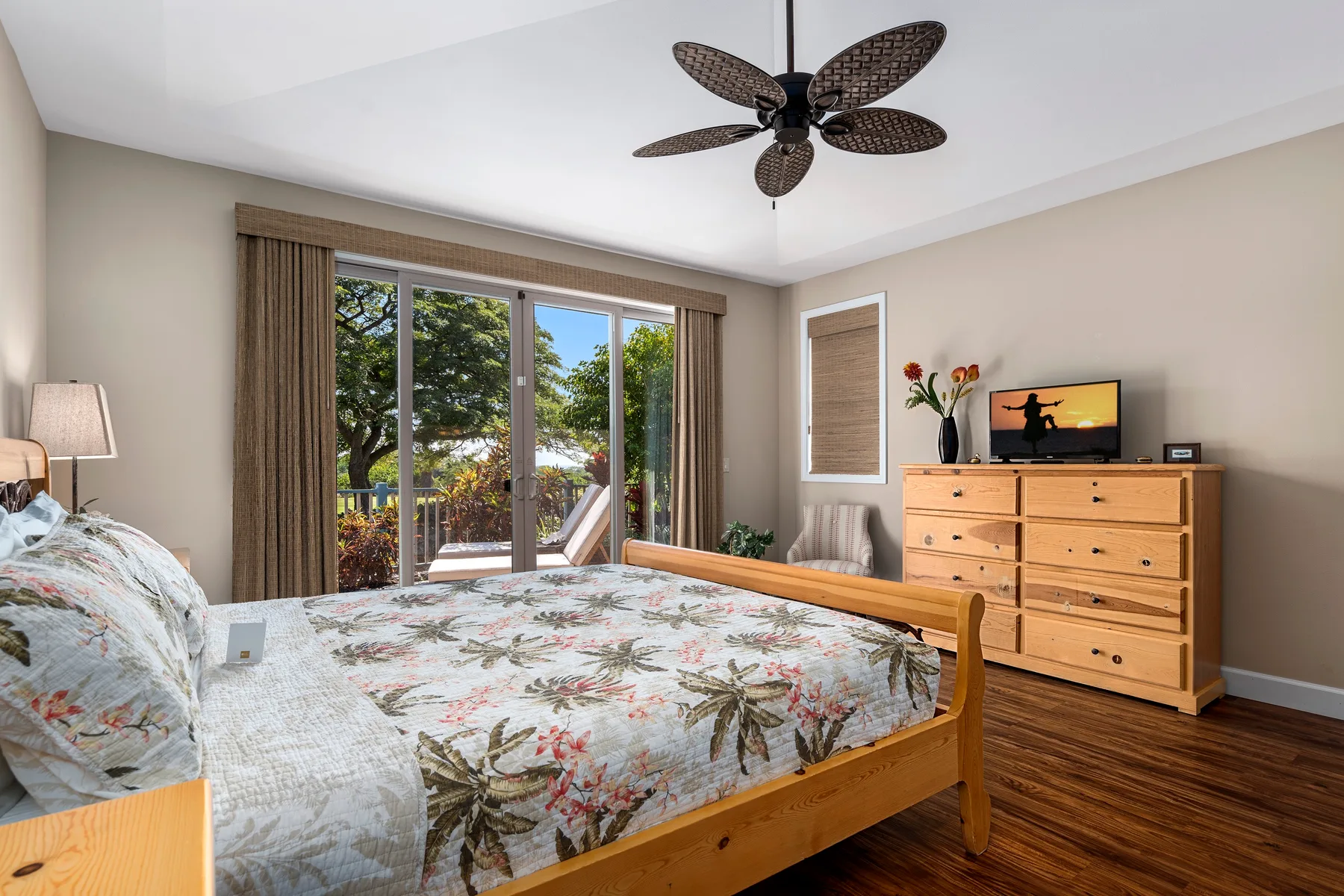 Un dormitorio con una cama de madera, ropa de cama floral y una cómoda junto a amplias ventanas.