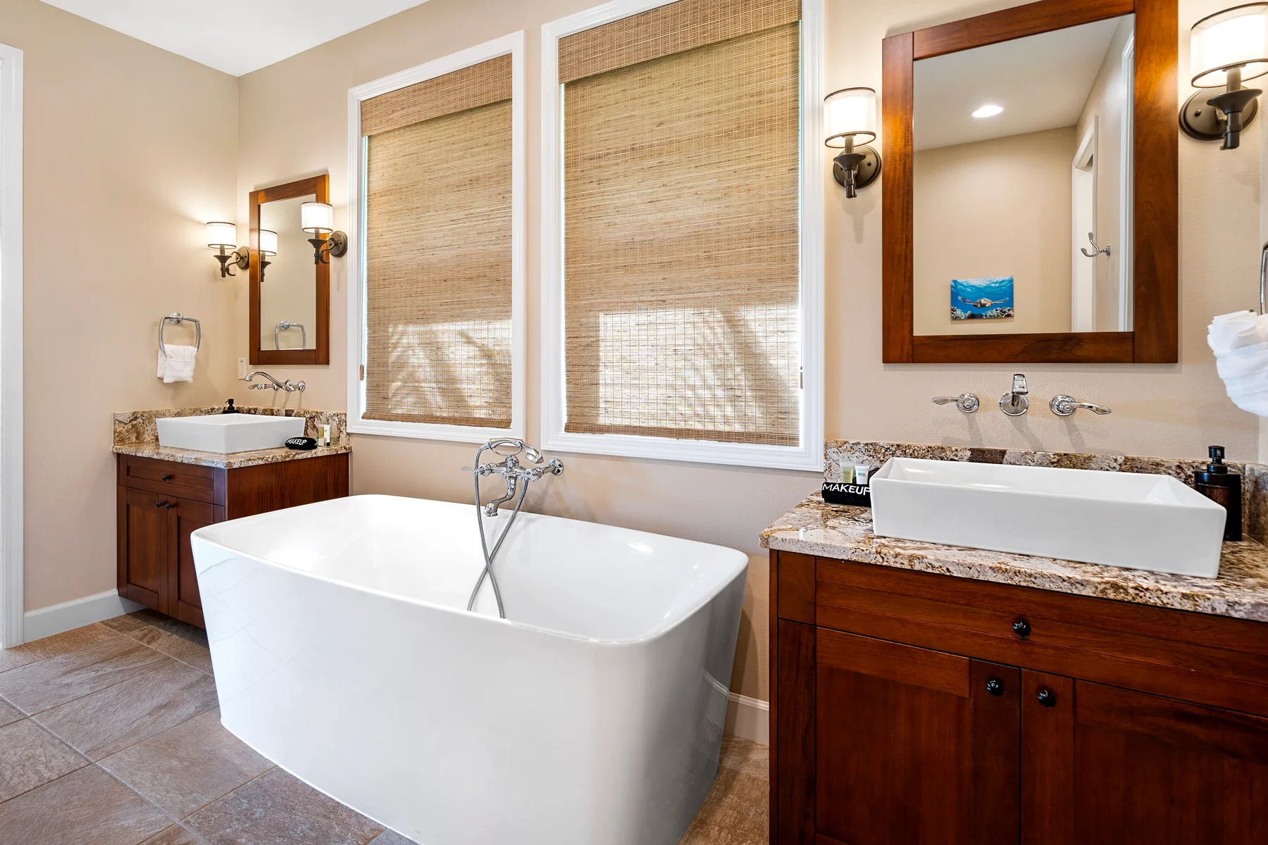 Un baño con bañera exenta, dos lavabos y ventanas con persianas tejidas.