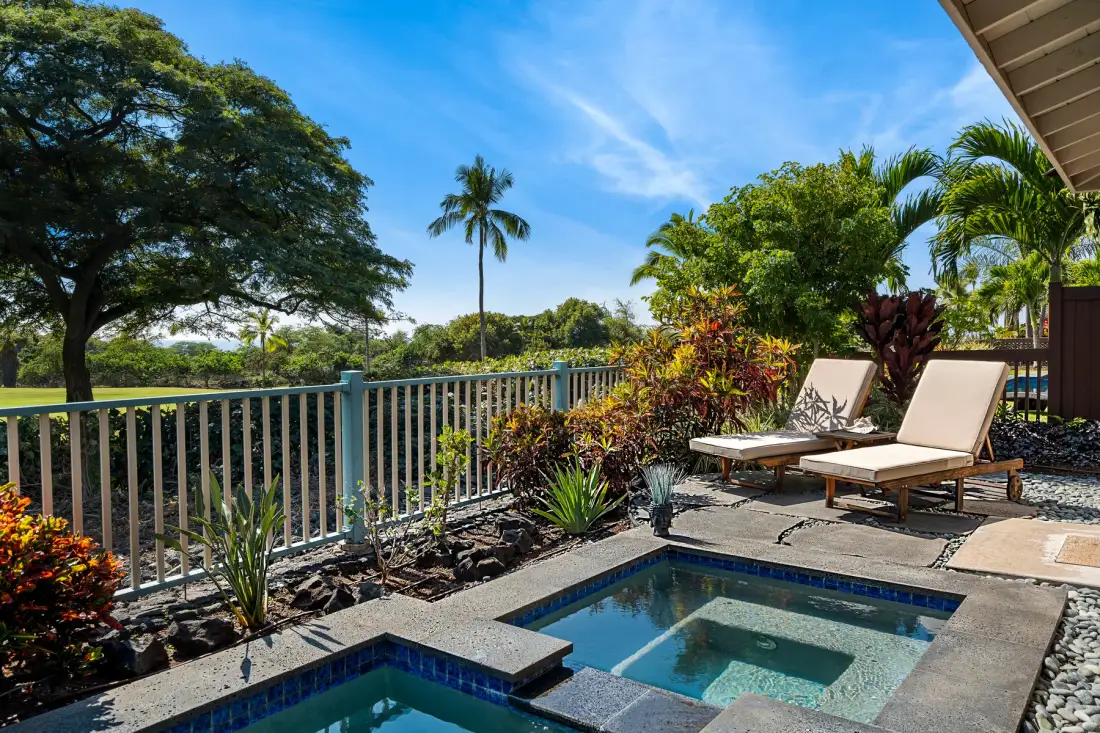 Una piscina y un spa al aire libre junto a un patio ajardinado con asientos.