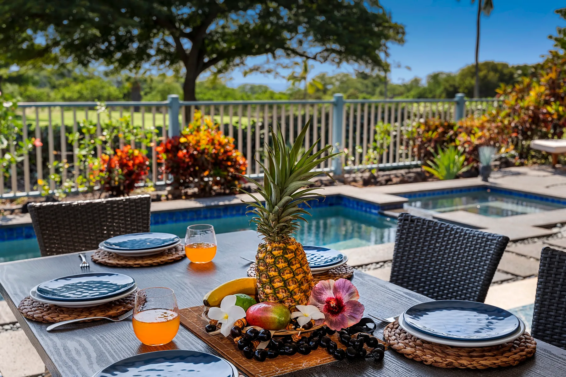 Una mesa junto a la piscina está puesta con platos, bebidas y una piña como centro de mesa.