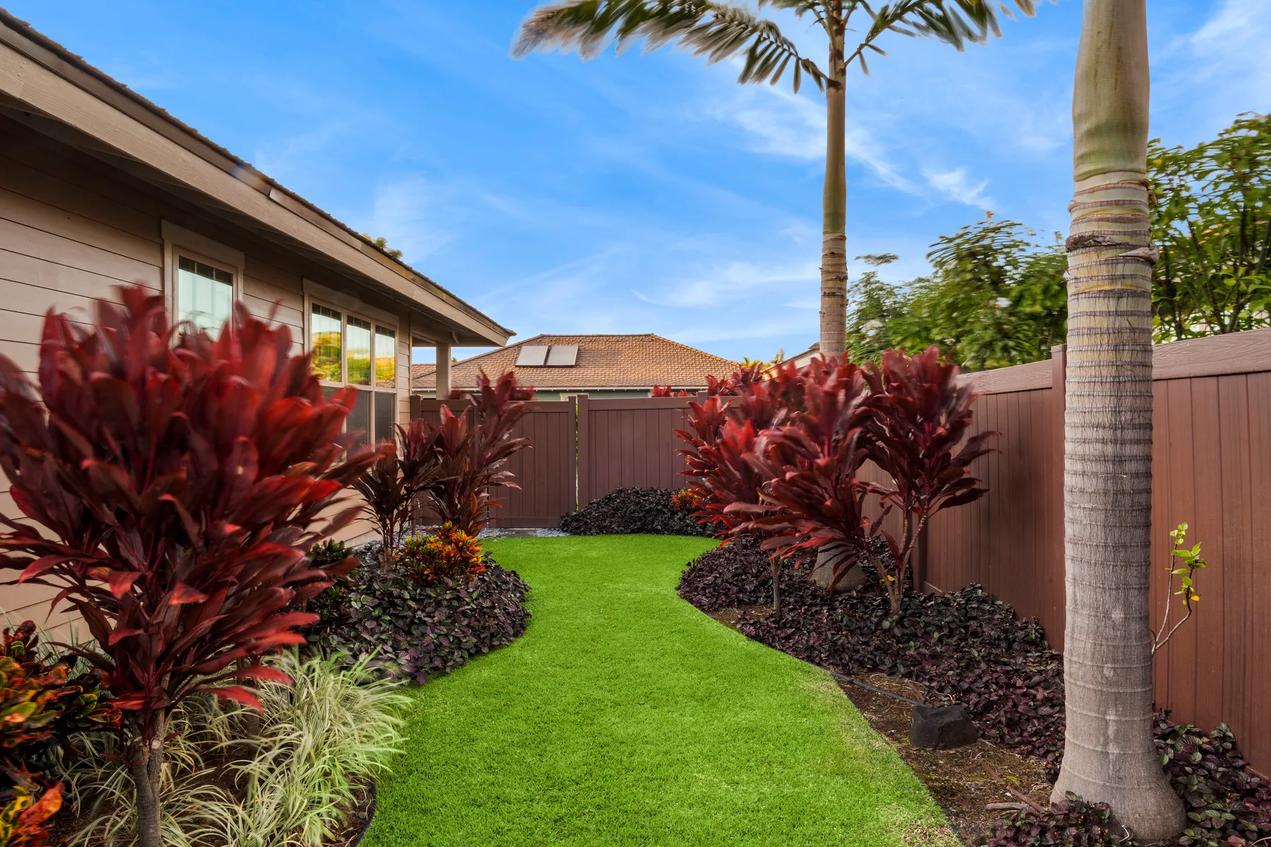 Un jardín cercado con césped verde, plantas tropicales y palmeras.