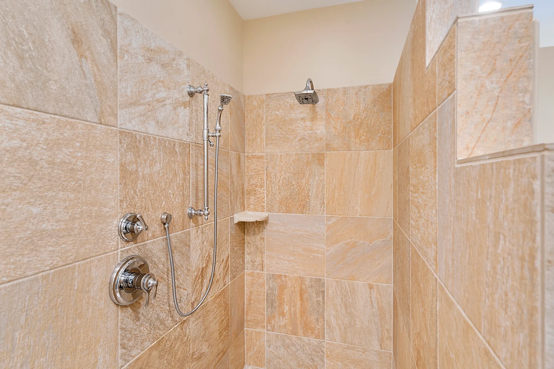 Una zona de ducha con azulejos, grifería de pared y una ducha de mano.