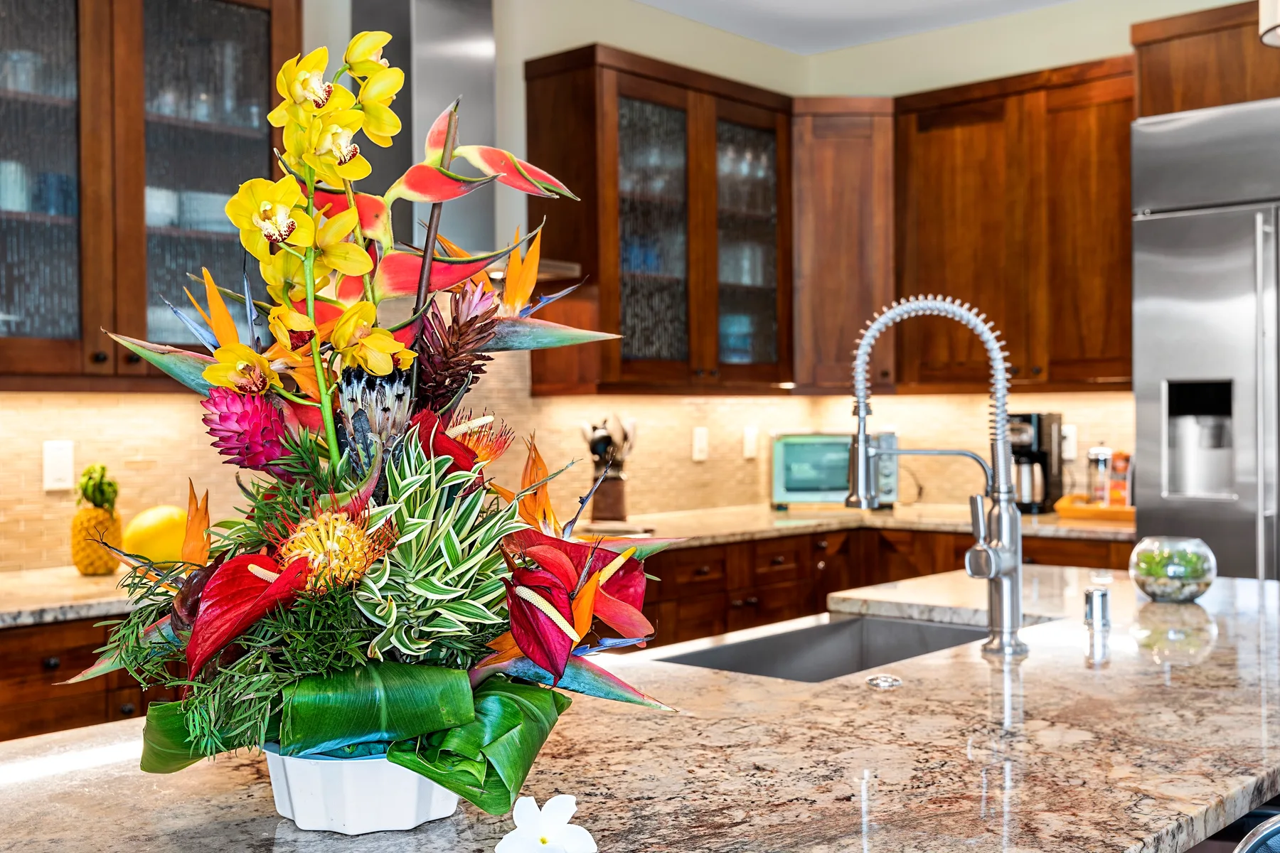 Una cocina con gabinetes de madera, una encimera de piedra y un arreglo floral colorido.