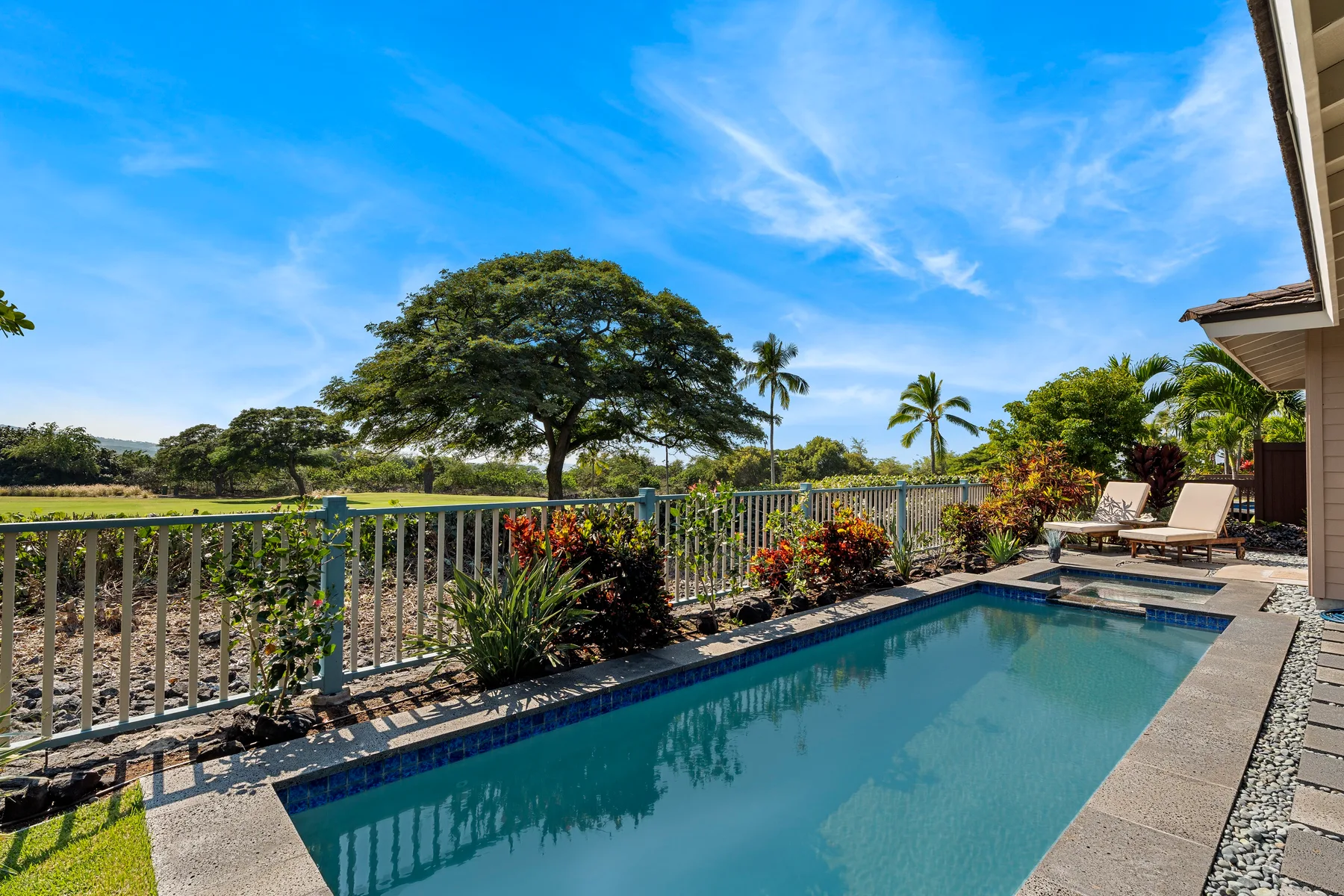 Una piscina al aire libre está bordeada por una barandilla y plantas tropicales.