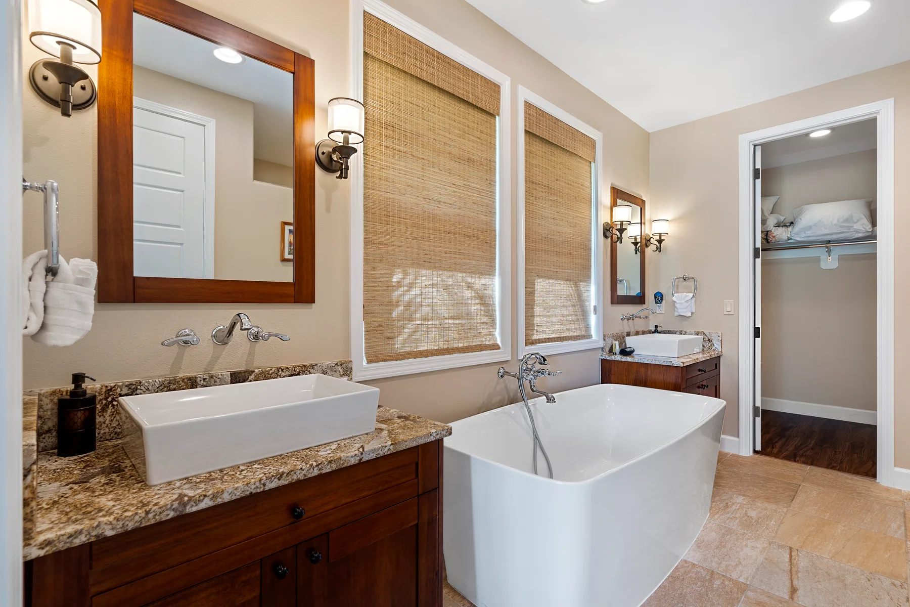 Un baño con lavabo, bañera exenta y ventanas con persianas tejidas.