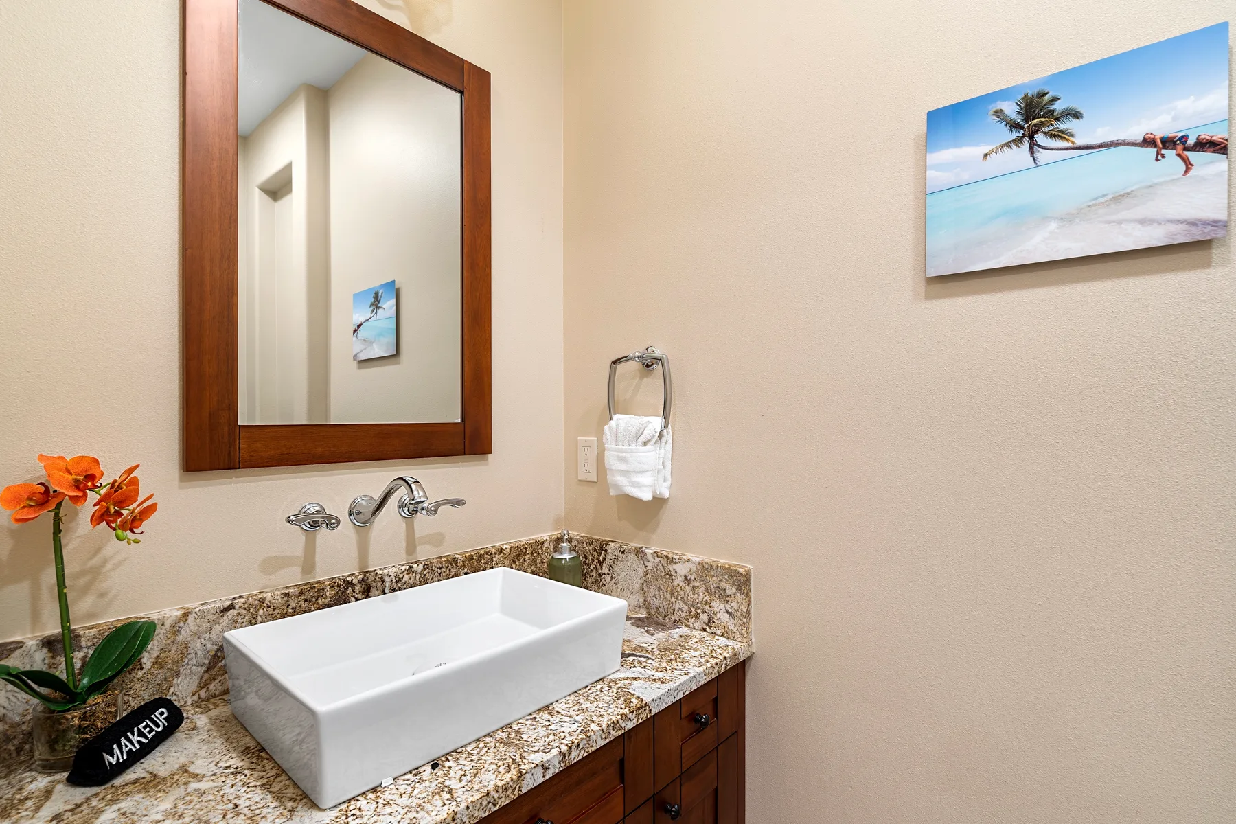 Un tocador de baño con lavabo de recipiente, espejo y cuadro de playa.