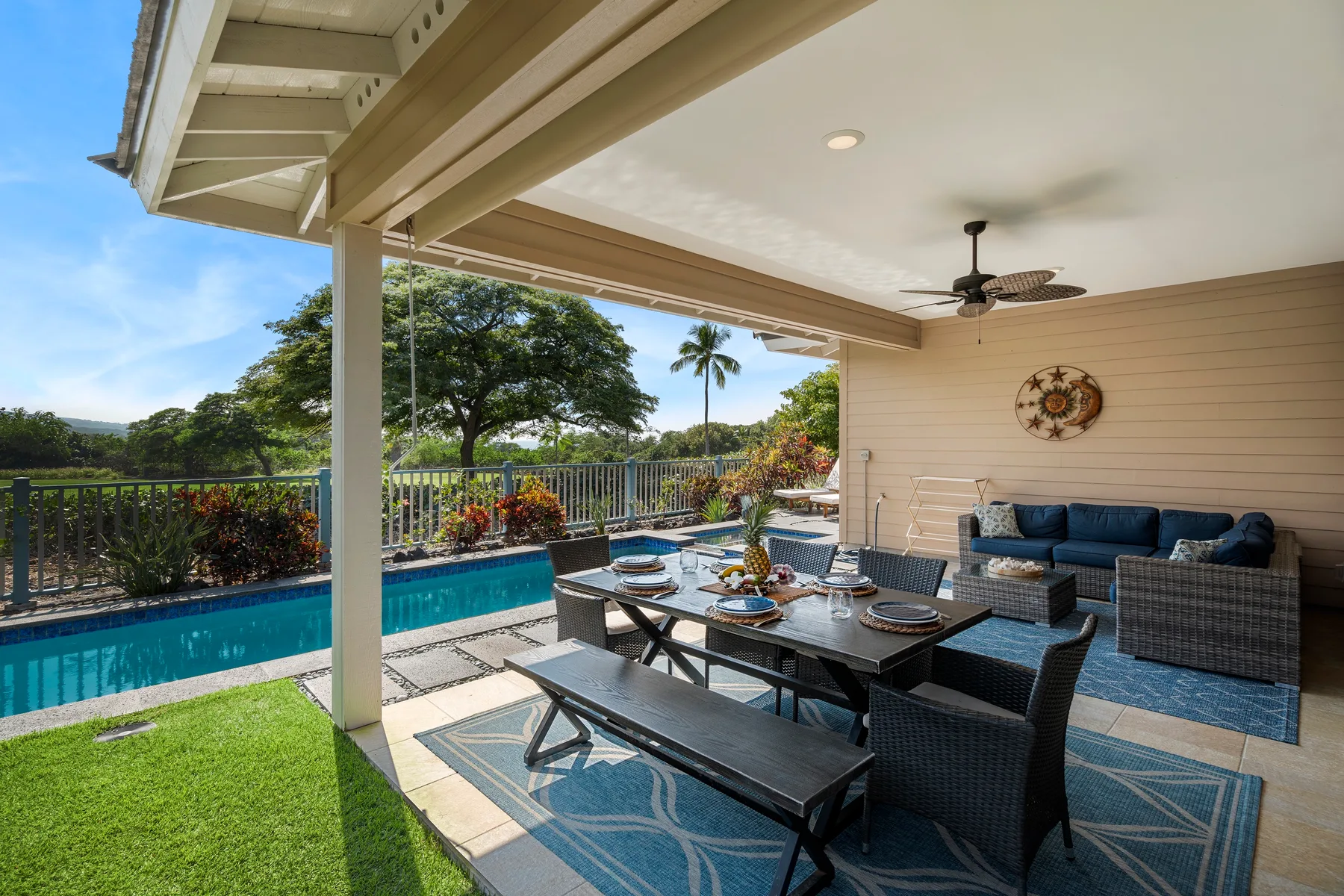 Un patio exterior cubierto tiene asientos para comer junto a una piscina y césped verde.