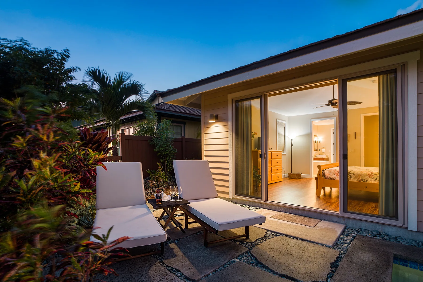 Un patio con asientos reclinables da a una habitación iluminada con puertas corredizas de vidrio.