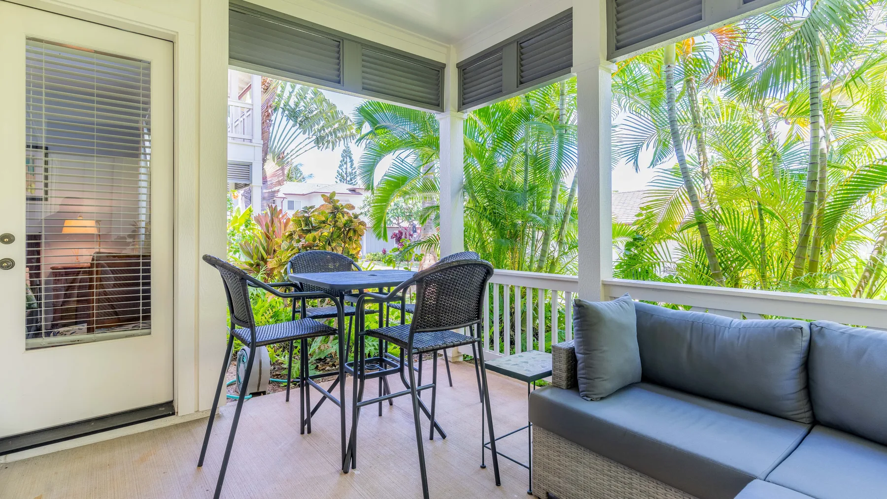 Un patio luminoso y cerrado con mesa, sillas y asientos acolchados junto a ventanas frondosas.