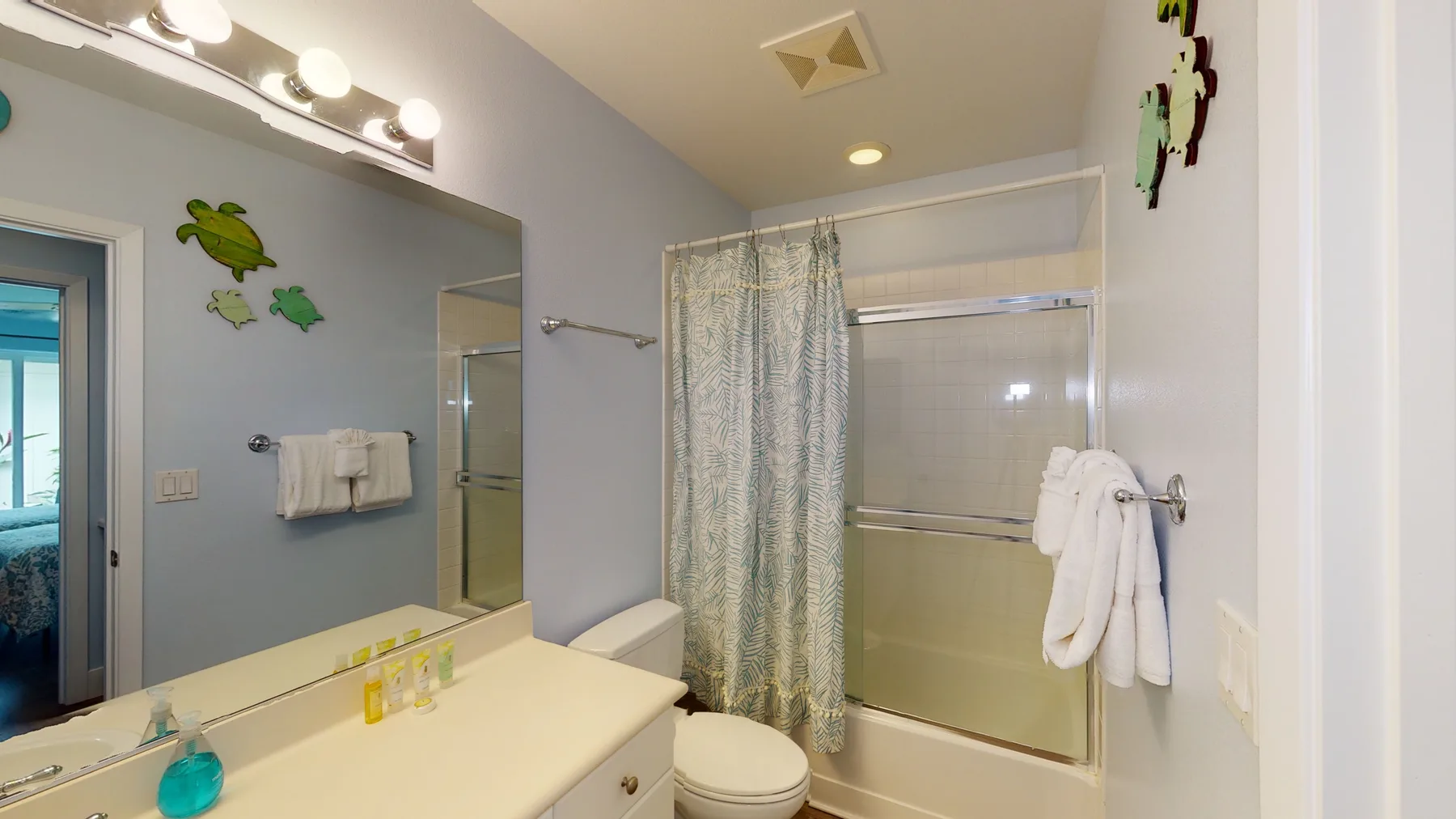 Un baño con un lavabo largo, un espejo y una bañera detrás de una cortina estampada.