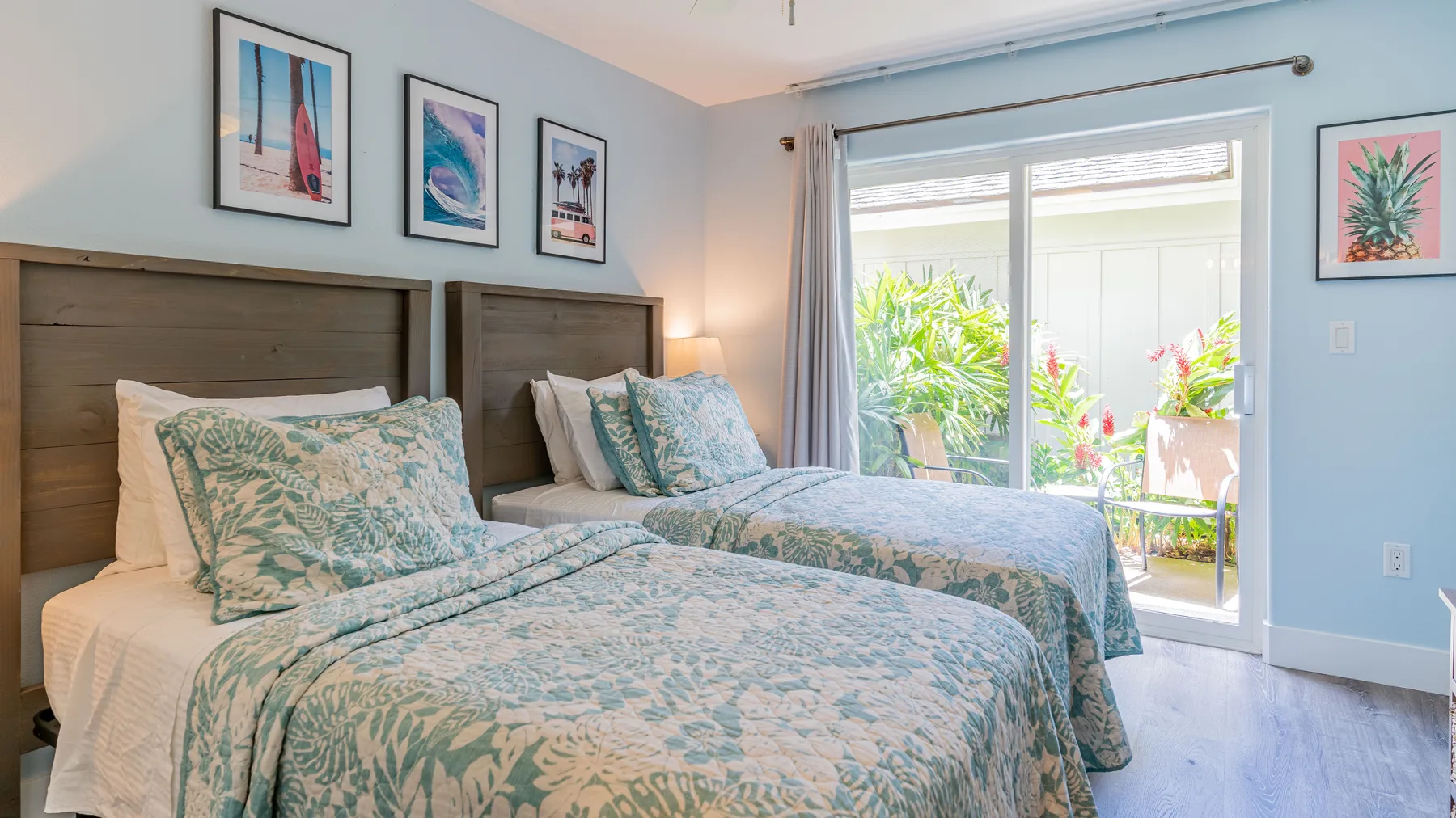 Un dormitorio con dos camas vestidas con ropa de cama azul pálido estampada junto a una puerta corrediza de vidrio.