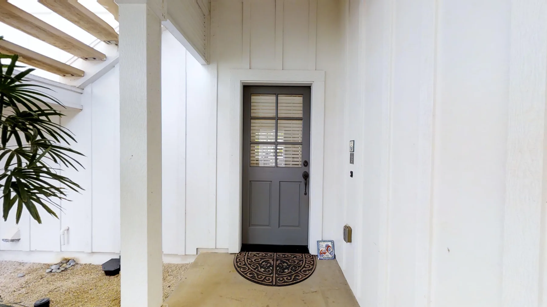 Una entrada blanca con una puerta gris y un felpudo estampado.