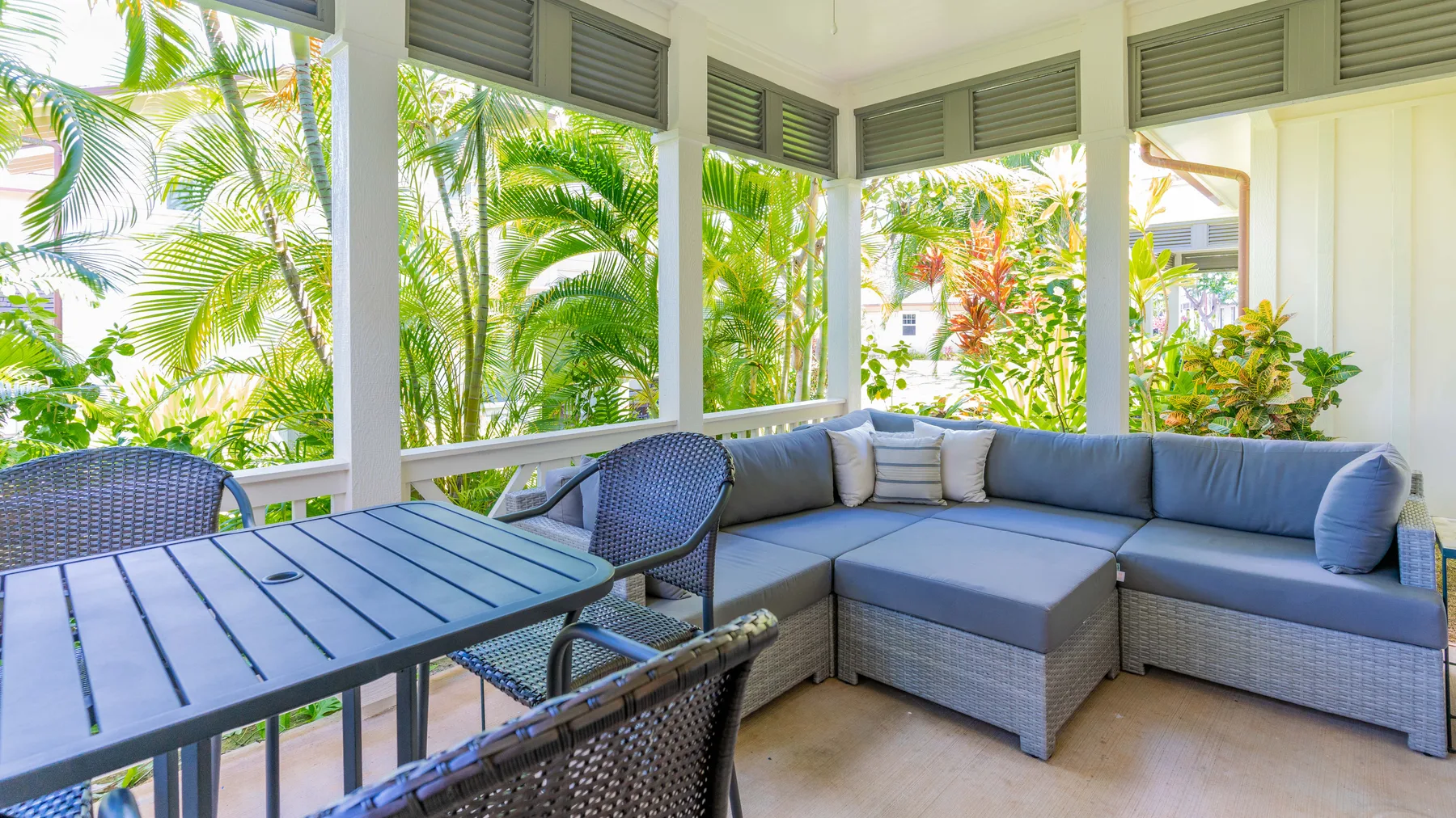 Un patio cubierto con una zona de asientos y una mesa de comedor junto a vegetación tropical.