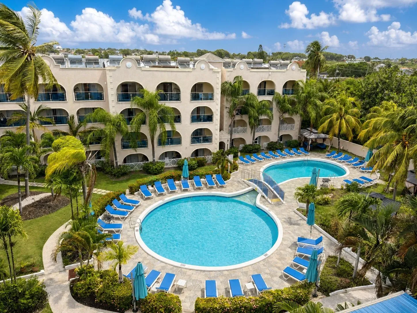 Hotel courtyard with outdoor pool, loungers, palm trees, and an arched building