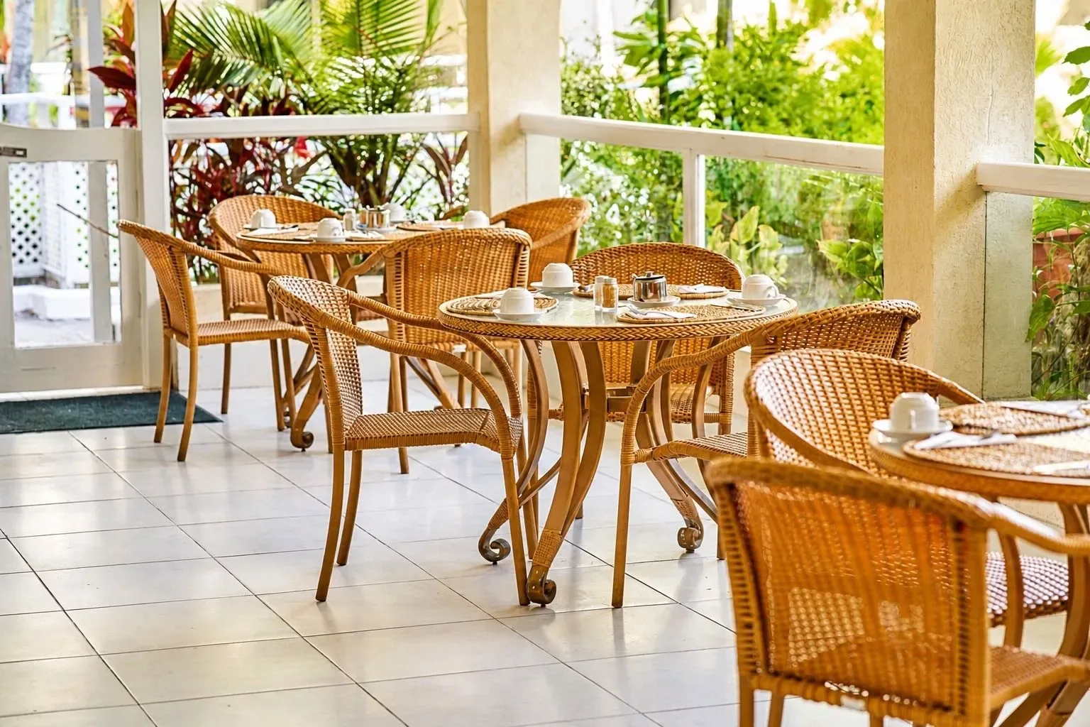 Terraza de cafetería al aire libre con mesas, sillas y plantas tropicales