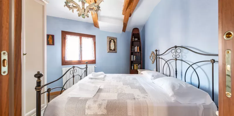 Un dormitorio con una cama de metal, paredes azul claro y vigas de madera a la vista.