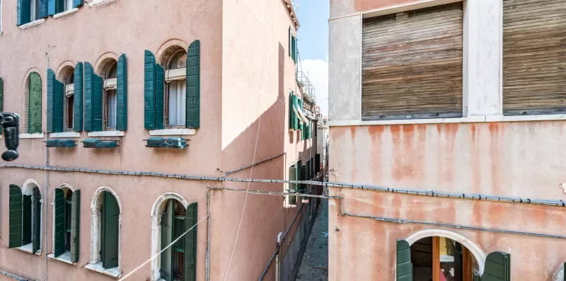 Edificios rosados con contraventanas verdes bordean una calle estrecha.