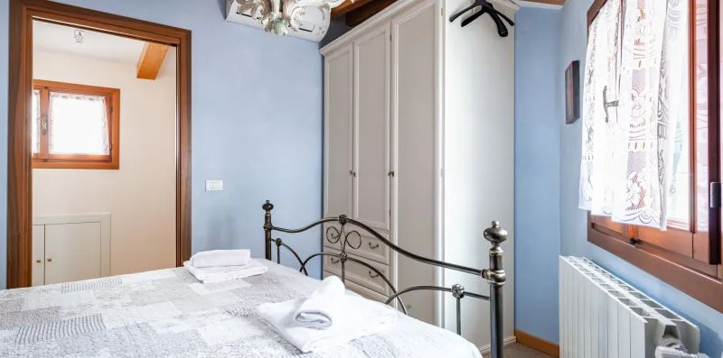 Un dormitorio con una cama de metal, toallas dobladas y una ventana.