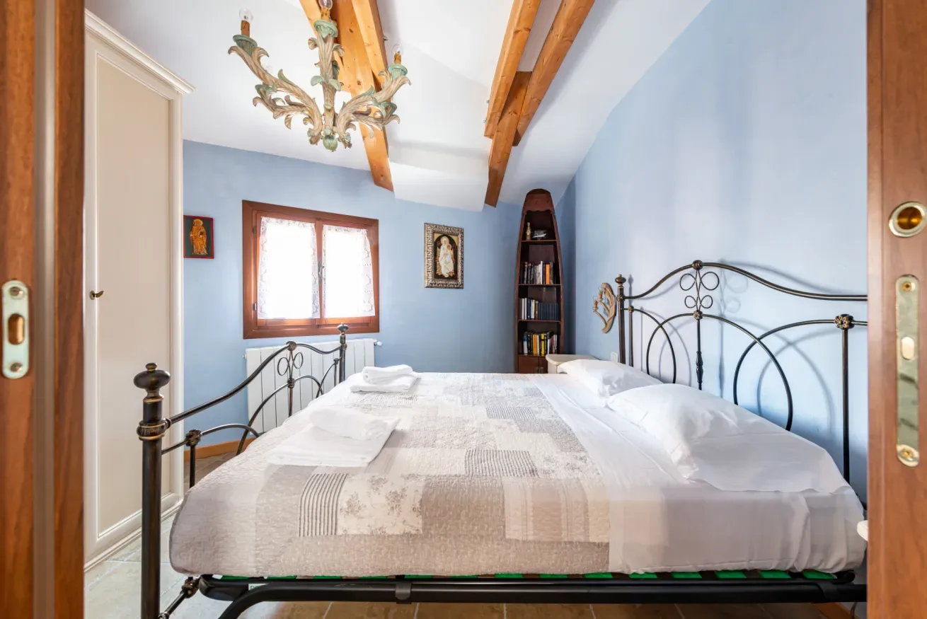 Un dormitorio con una cama de metal, ropa de cama clara y una ventana.
