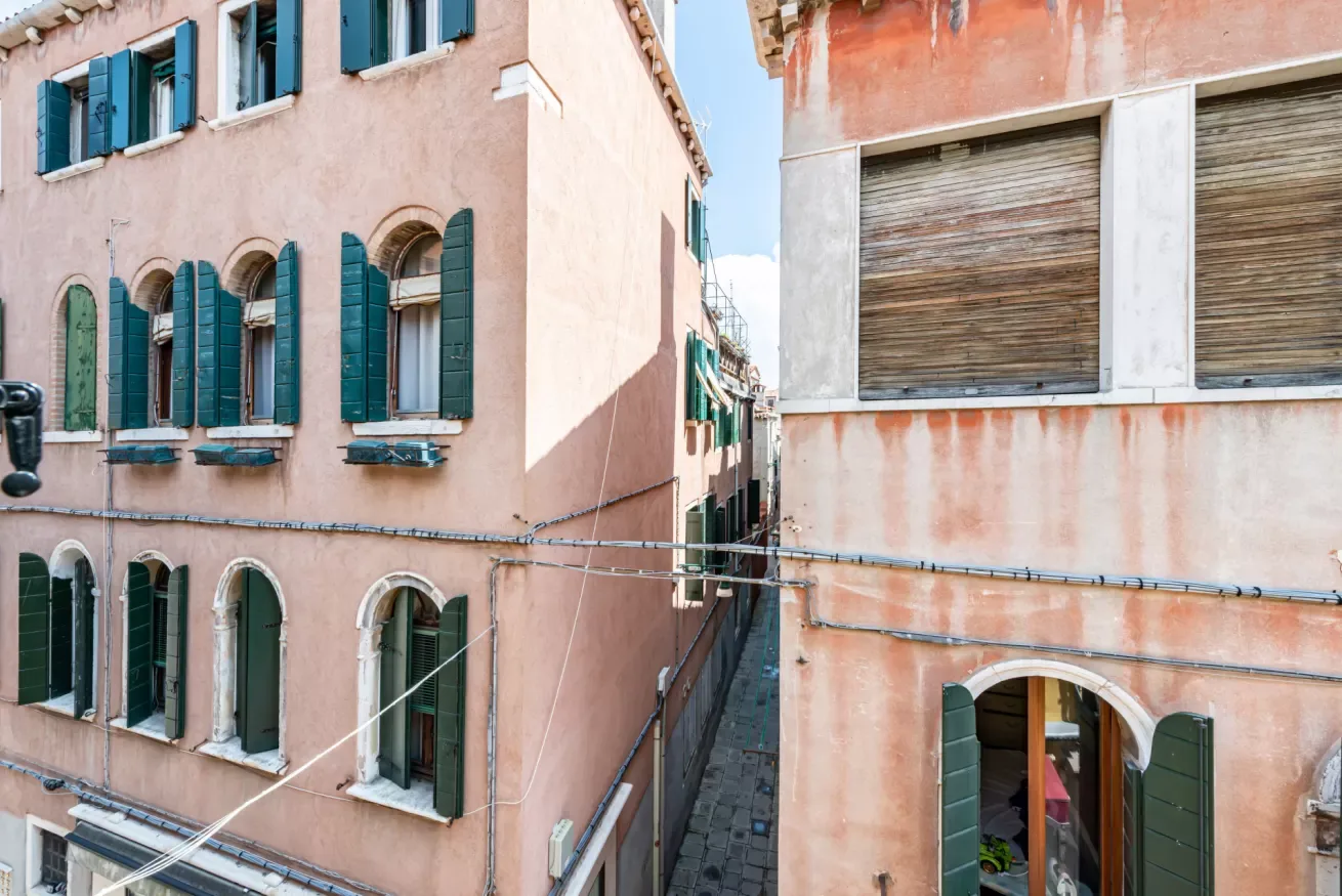 Un callejón estrecho pasa entre edificios rosados con persianas verdes.