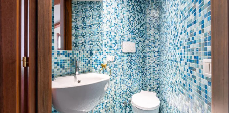 Un baño alicatado con lavabo de pared e inodoro.