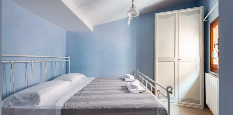 Un dormitorio con una cama, paredes azul claro y un armario blanco alto.