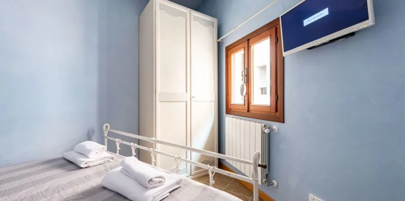 Un dormitorio con una cama, toallas dobladas, un armario y una ventana.