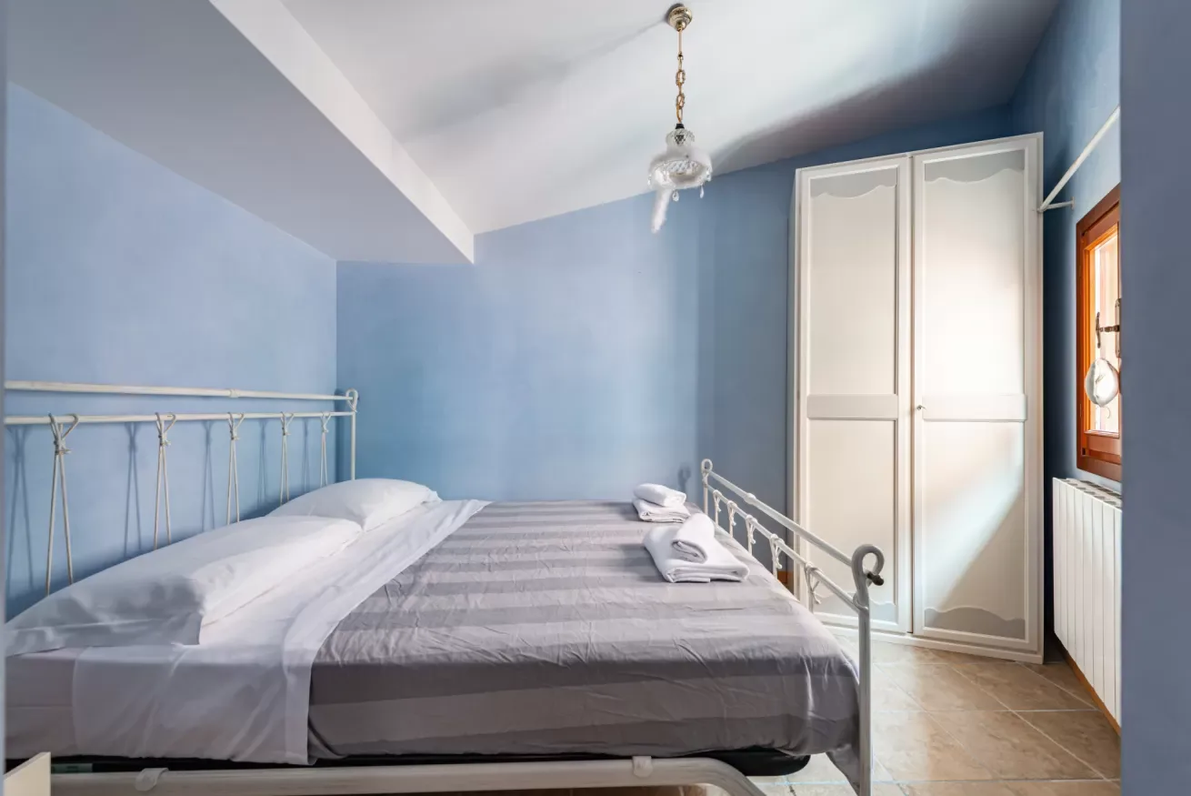 Un dormitorio con una cama junto a un armario blanco alto y una ventana.