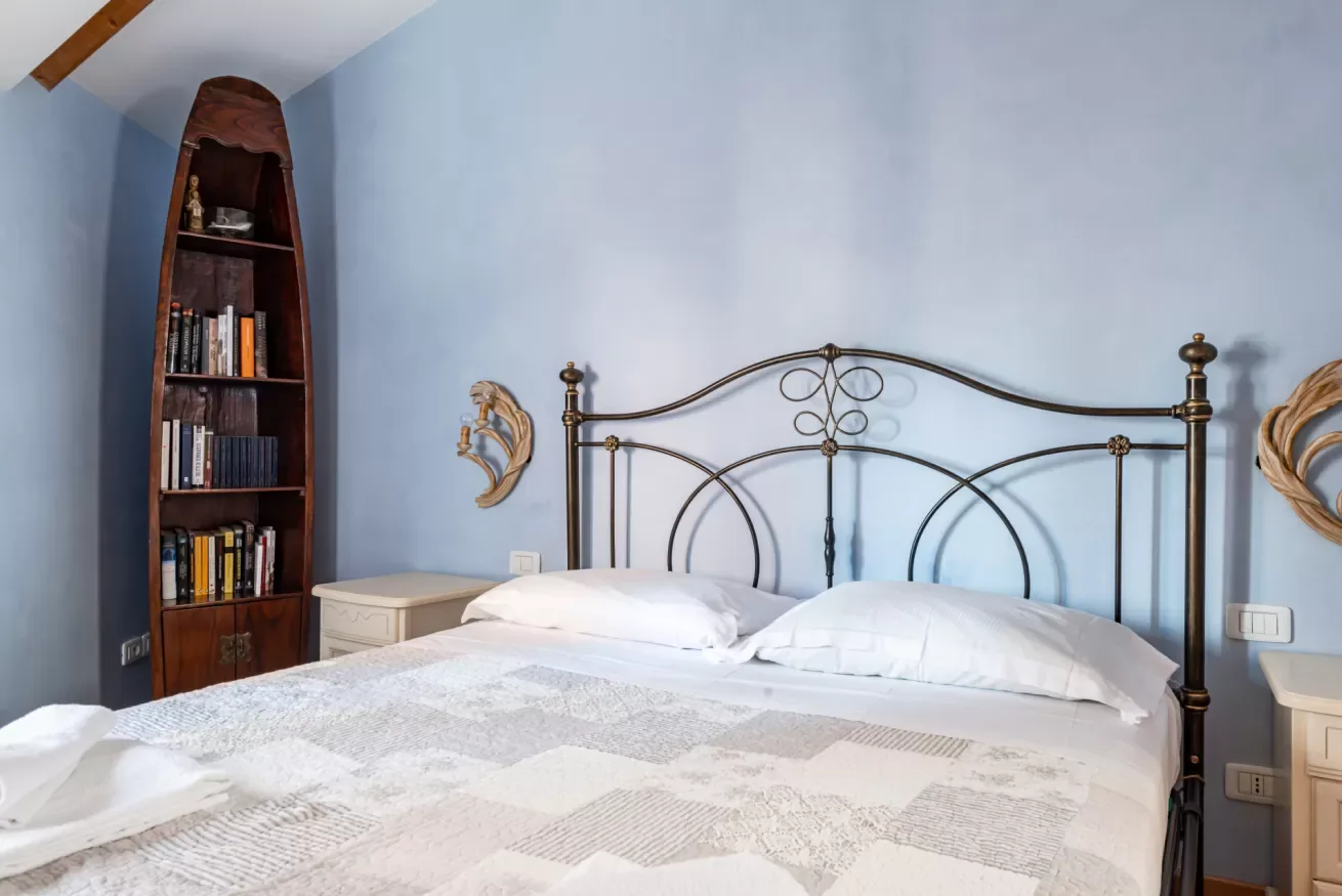 Un dormitorio con una cama, una colcha estampada y una estantería alta junto a una pared azul.