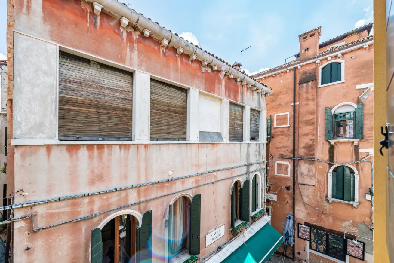 Un patio estrecho está rodeado de edificios rosados con ventanas con persianas.