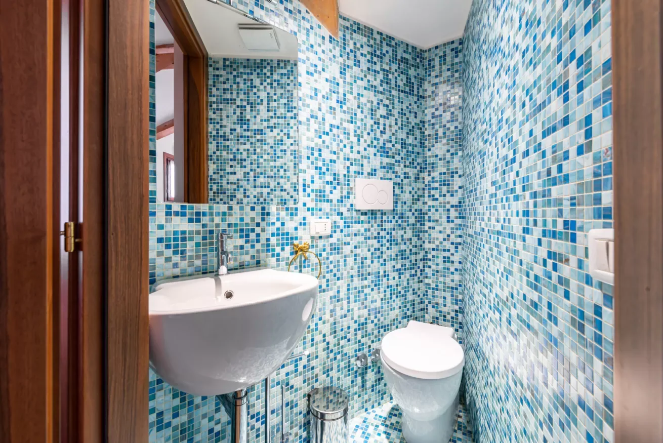 Un baño pequeño con mosaicos azules, un lavabo suspendido y un inodoro.