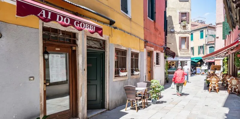 Una calle peatonal estrecha con edificios coloridos y mesas de café al aire libre.