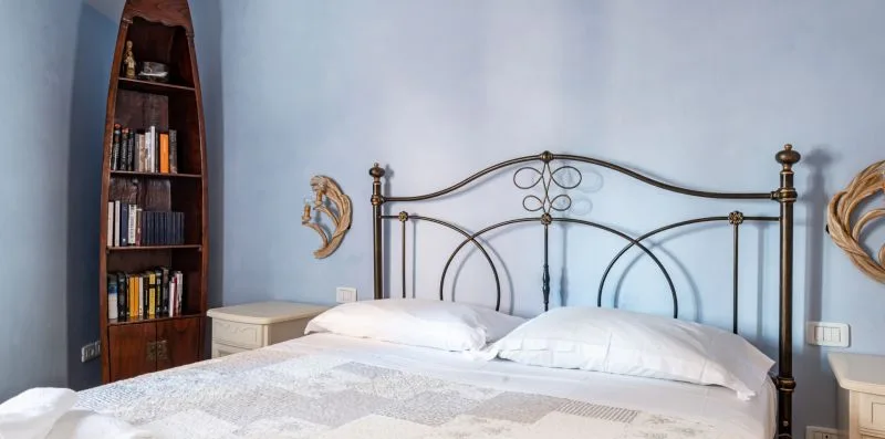 Un dormitorio con una cama, paredes azul claro y una estantería alta.