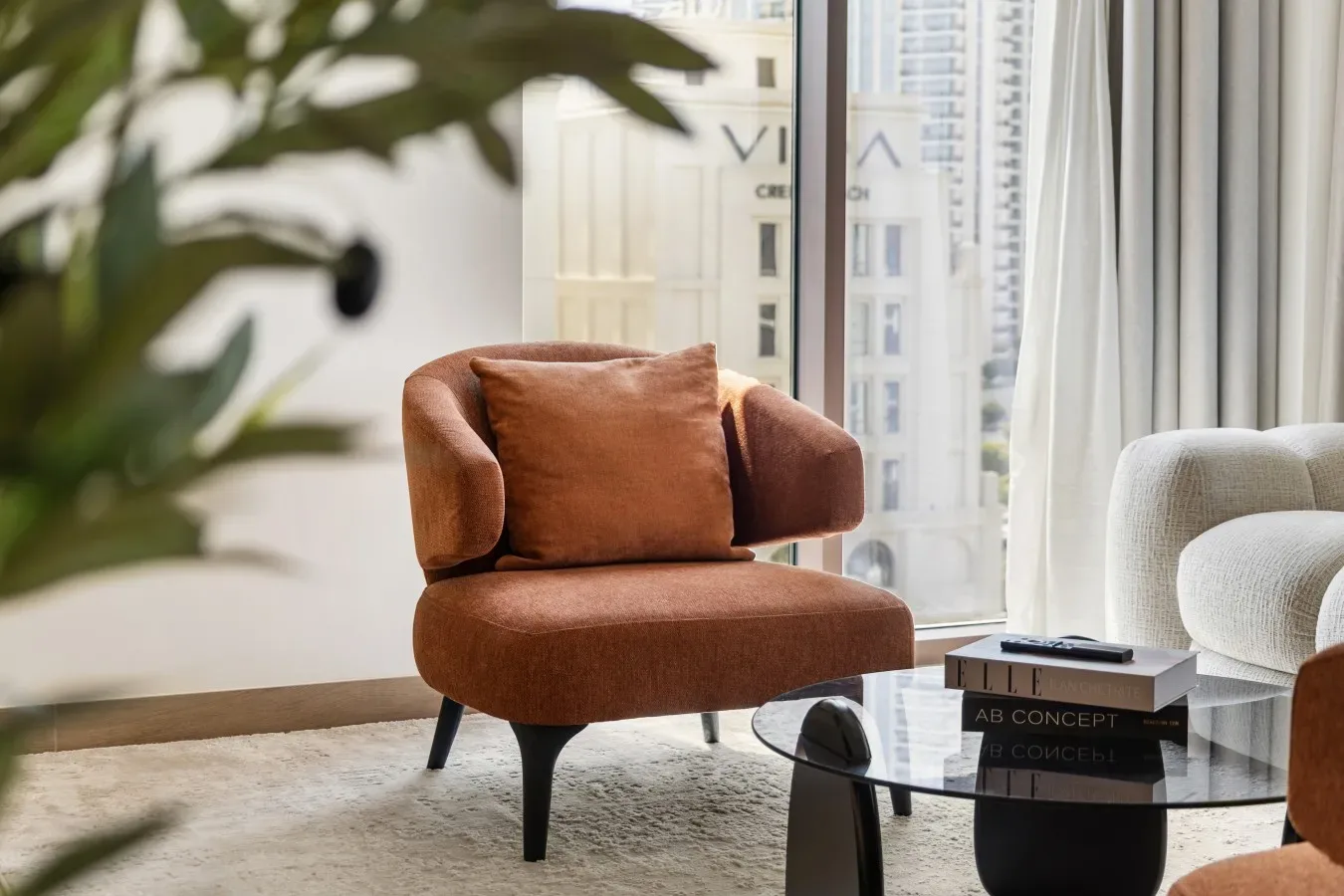 Una zona de estar con un sillón color óxido junto a una mesa de centro de vidrio.