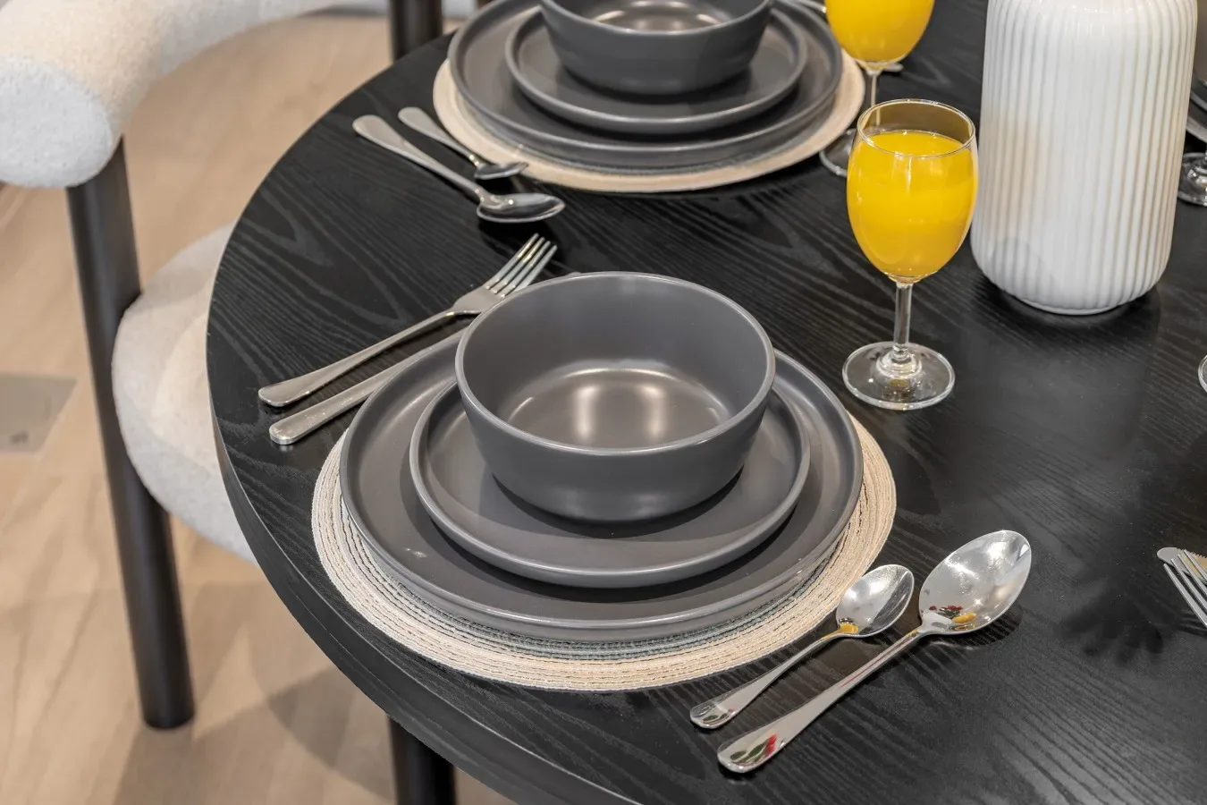 Una mesa de comedor está puesta con platos grises, cubiertos y vasos de jugo de naranja.
