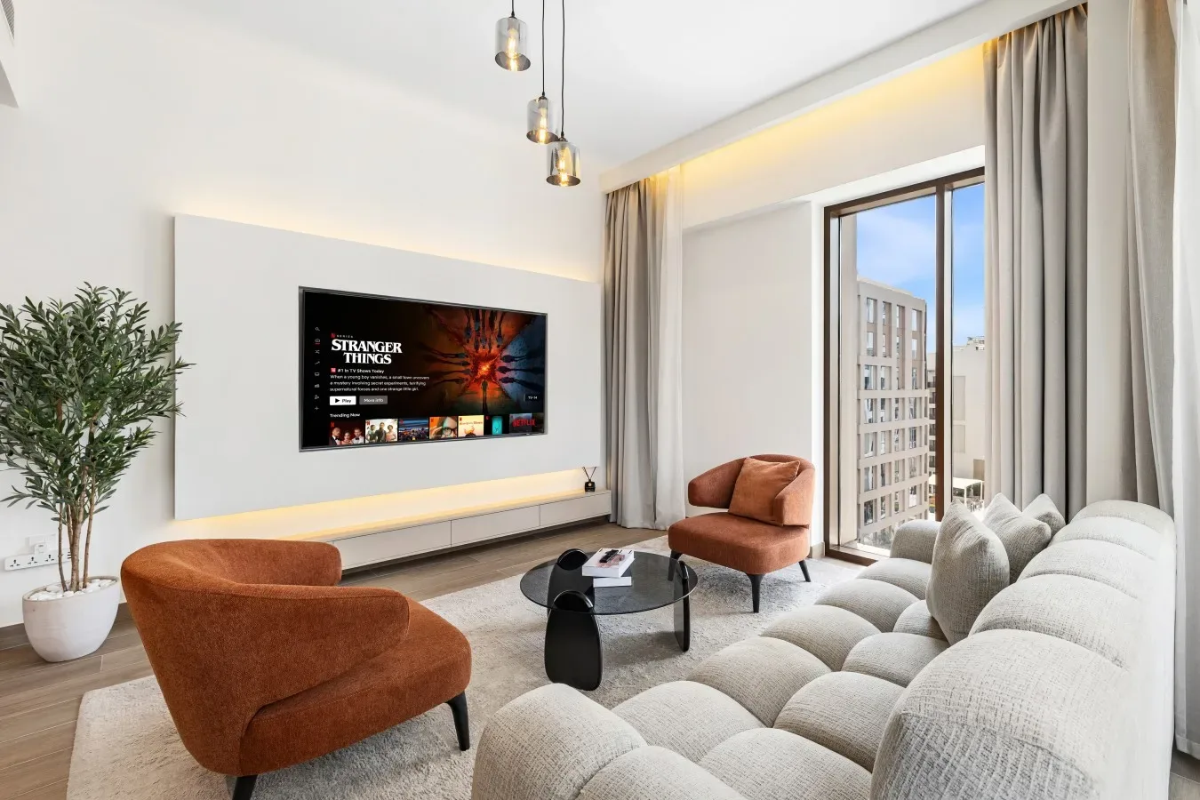 Una sala de estar moderna con televisor, asientos y ventanas grandes.