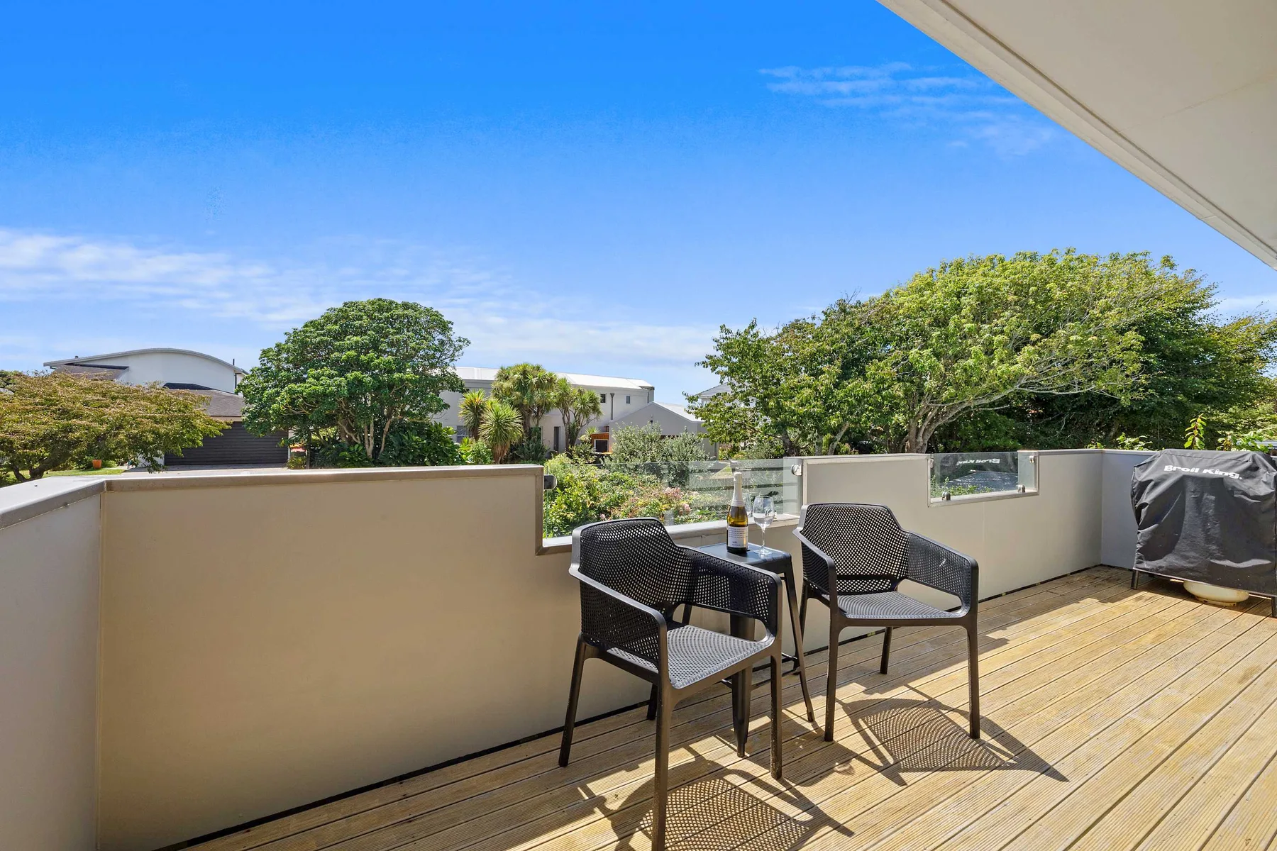 Una terraza soleada al aire libre con asientos y vista a árboles frondosos.