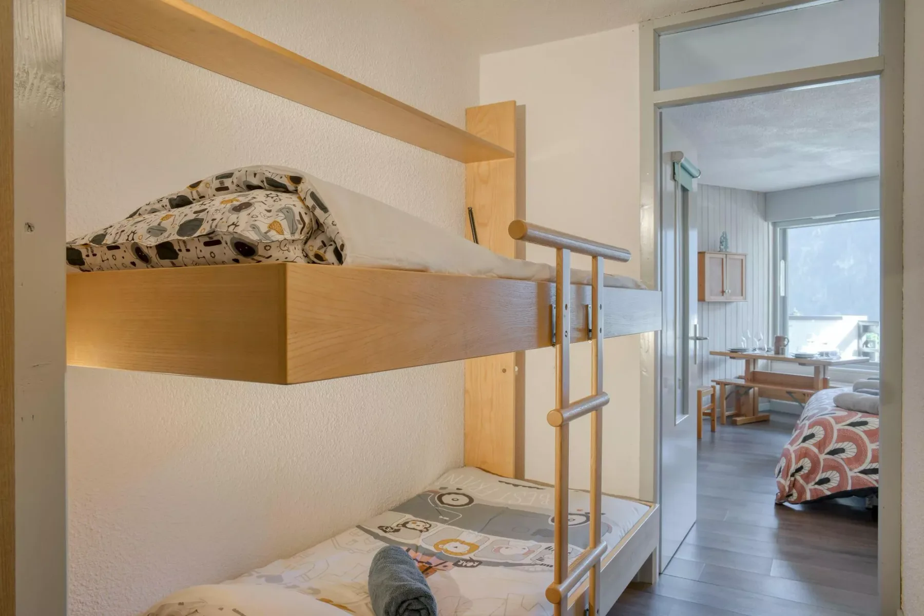 A bunk bed with patterned bedding stands beside an open doorway to a sitting area.
