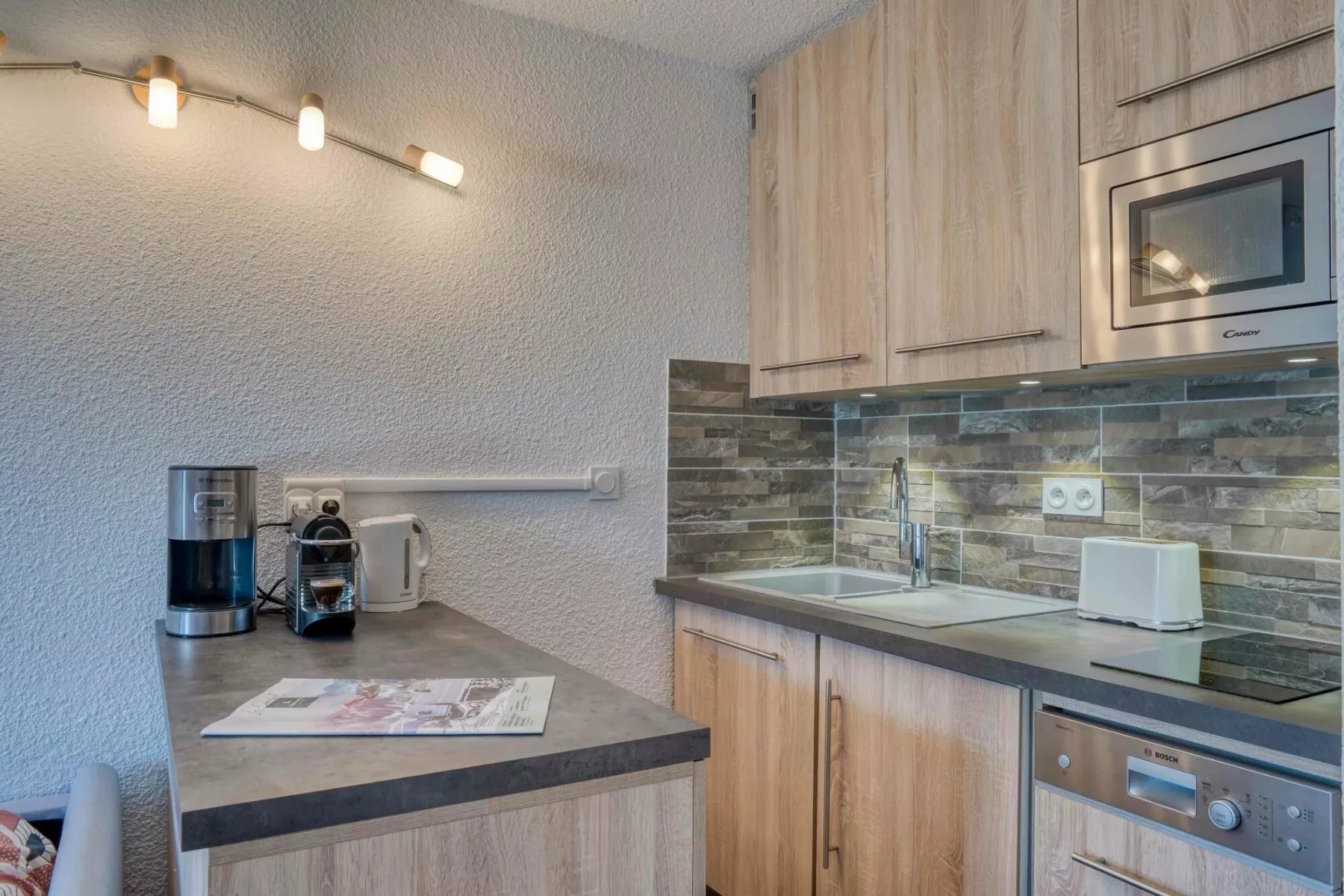 A compact kitchen with wood cabinetry, a tiled backsplash, and countertop appliances.