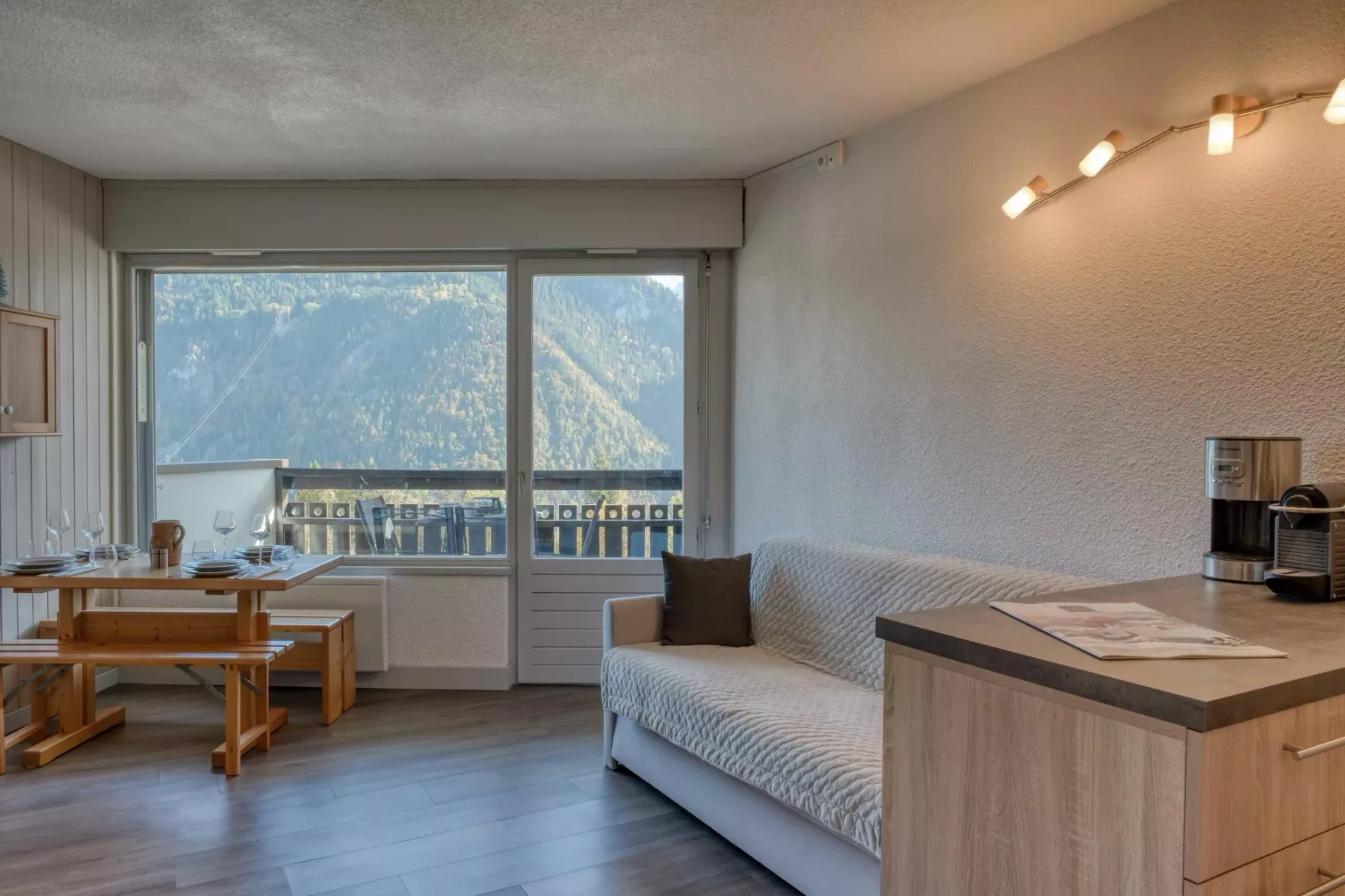 A sitting area with a sofa, dining table, and large windows overlooking a mountain view.