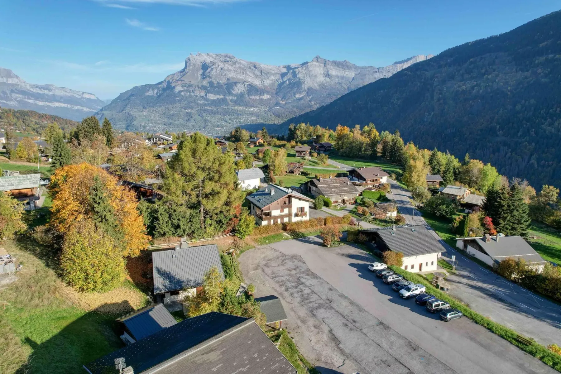 An aerial view of a mountain village with homes, roads, and autumn trees.
