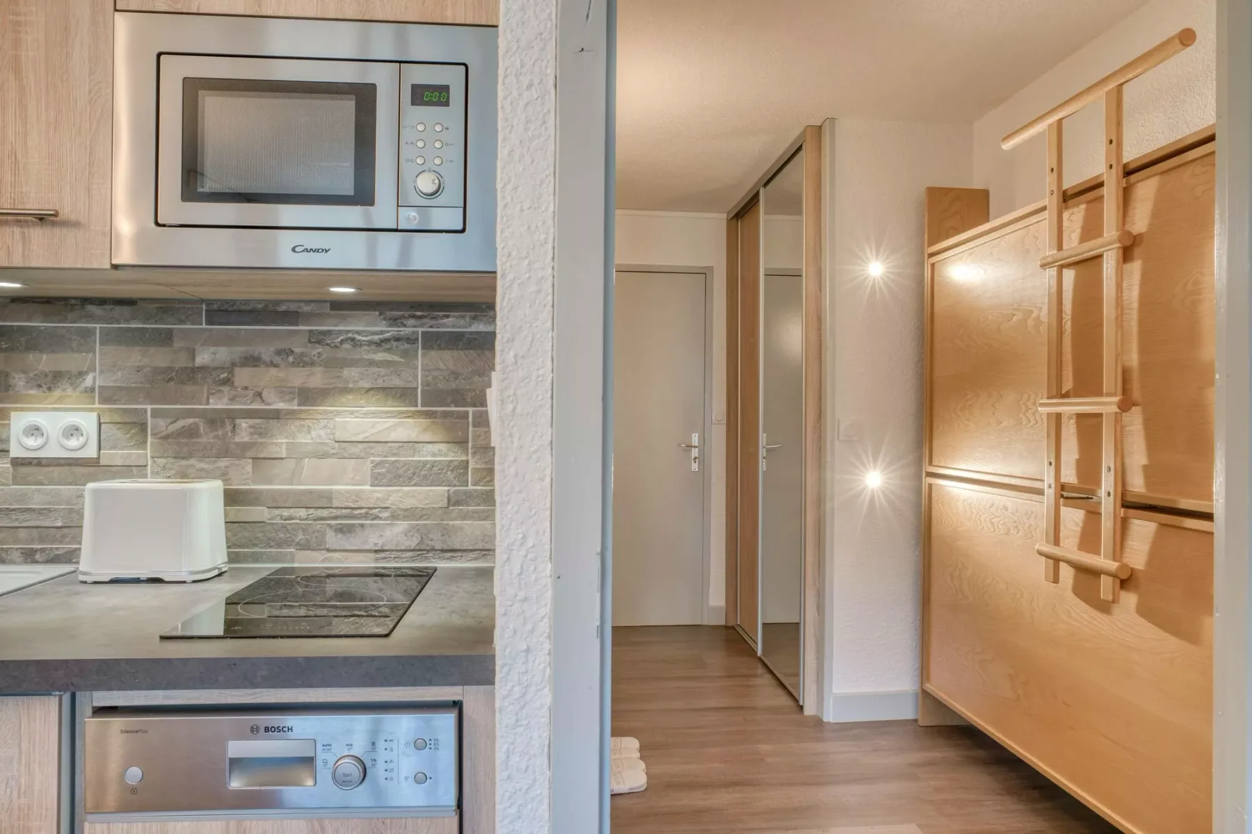 A compact kitchen opens onto a hallway, with wooden storage along the wall.