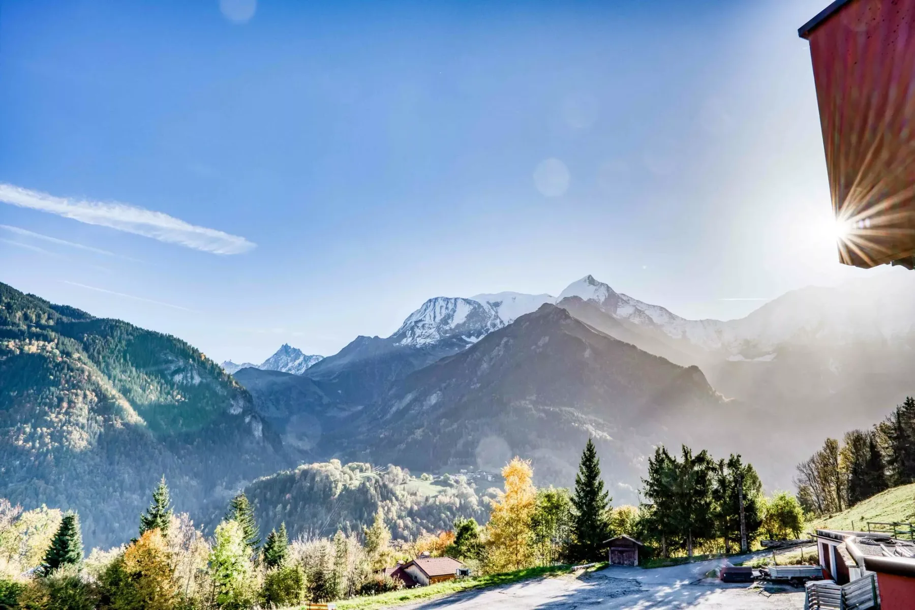 Mountain scenery fills the view beneath a clear sky, with trees and a building edge nearby.