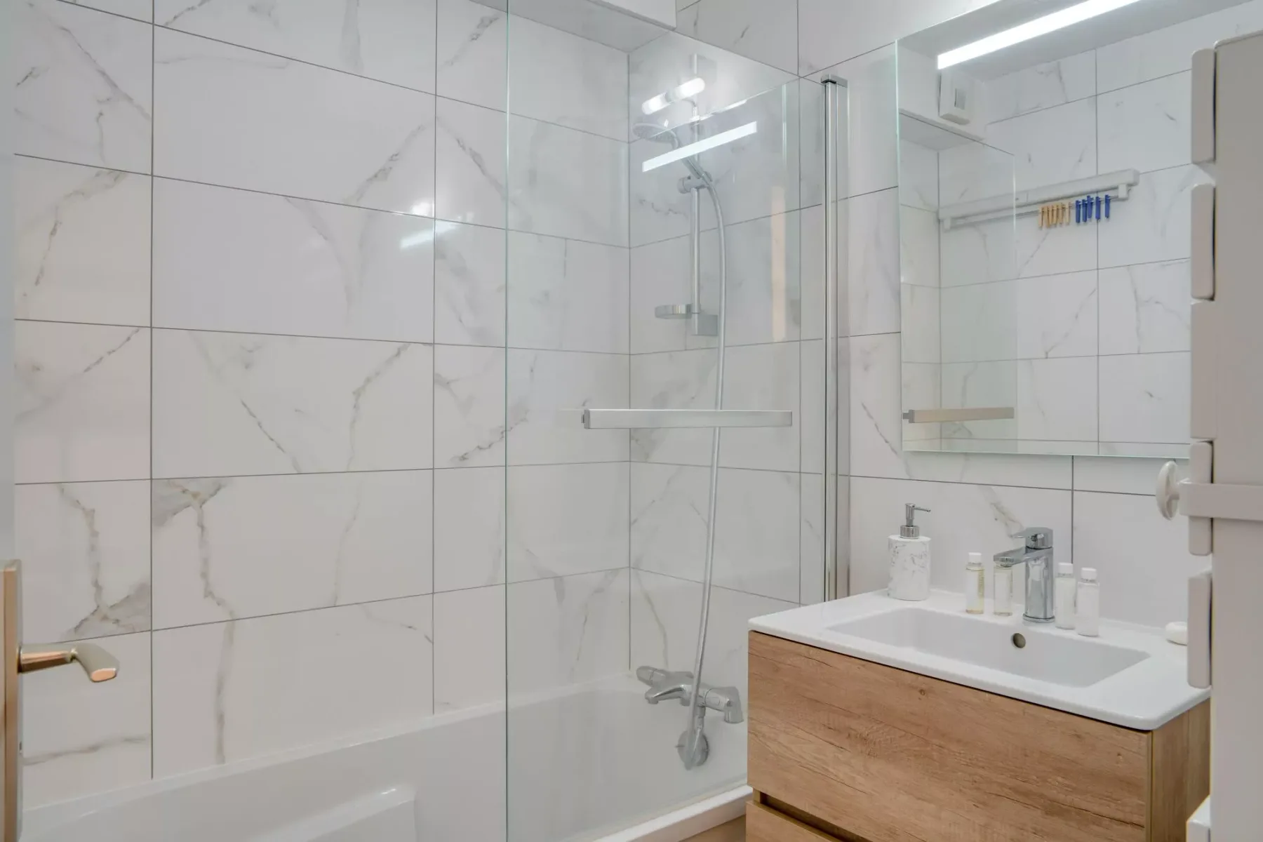 A tiled bathroom with a glass shower and a wood-fronted vanity.